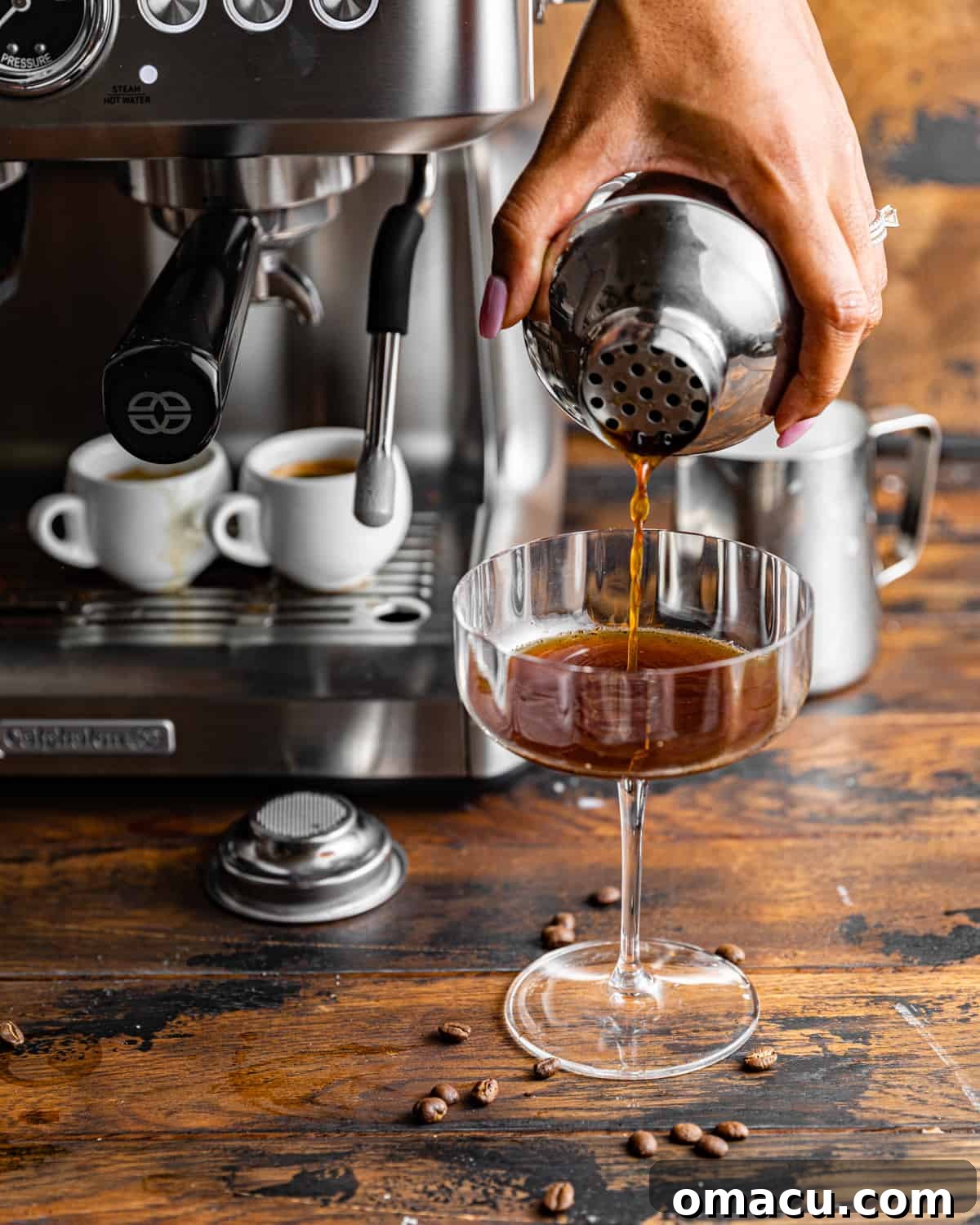 A hand pouring a freshly shaken espresso martini from a cocktail shaker into a chilled martini glass.