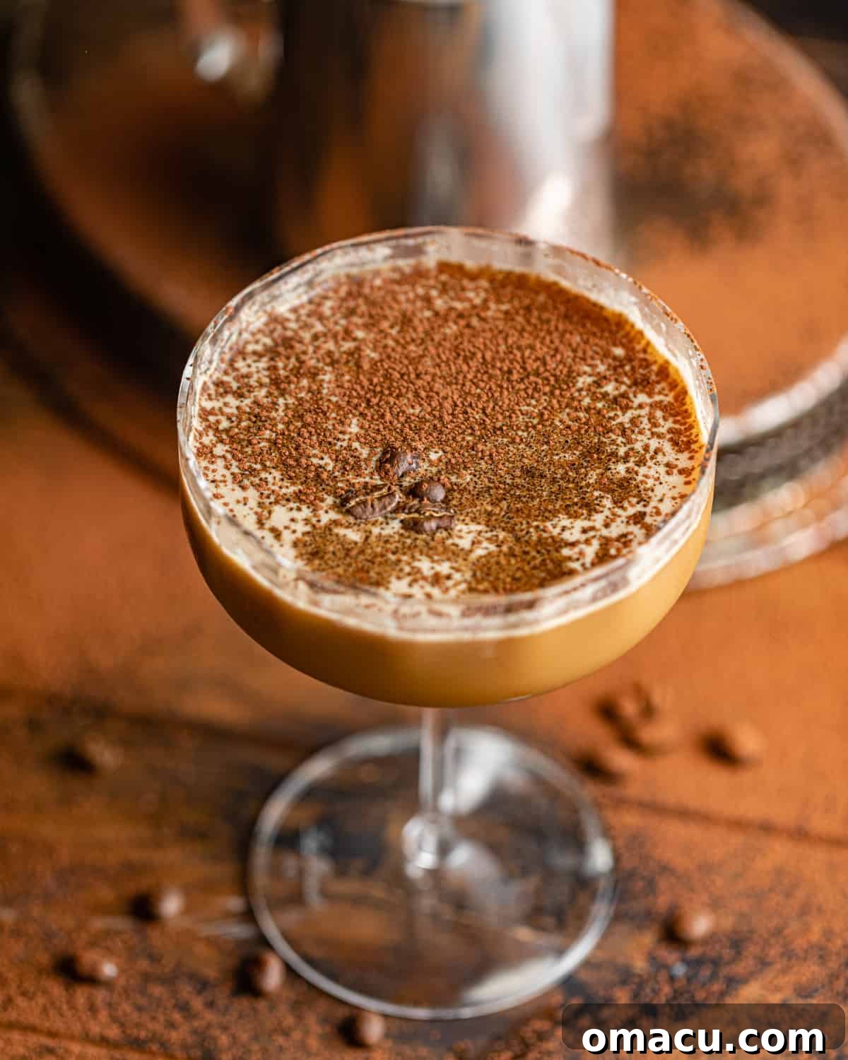 A close-up of a frothy espresso martini in a martini glass, garnished with three coffee beans.