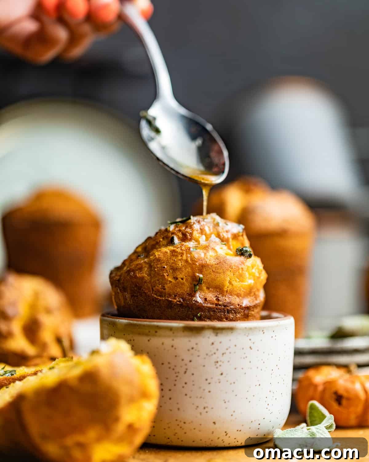 A golden-brown pumpkin popover, perfectly risen, served in a small white bowl with melted butter drizzled over it.