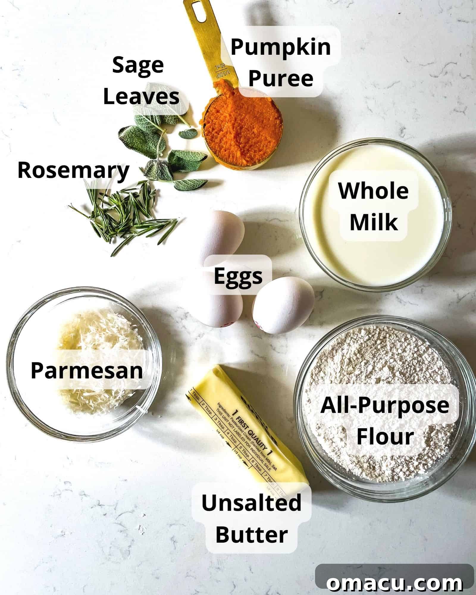 Ingredients laid out on a kitchen counter for making pumpkin popovers: flour, whole milk, grated parmesan, melted butter, pumpkin puree, large eggs, fresh rosemary sprigs, fresh sage leaves, and kosher salt.