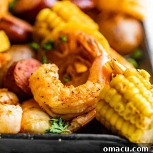 a piece of shrimp on a plate with corn, sausage, and potatoes.