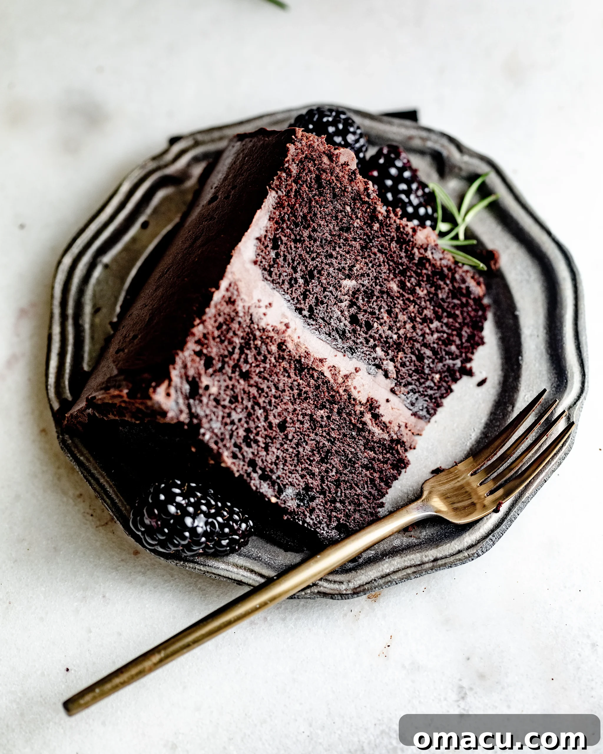 A perfectly cut slice of chocolate ganache cake on a white plate, revealing the moist layers and generous frosting.
