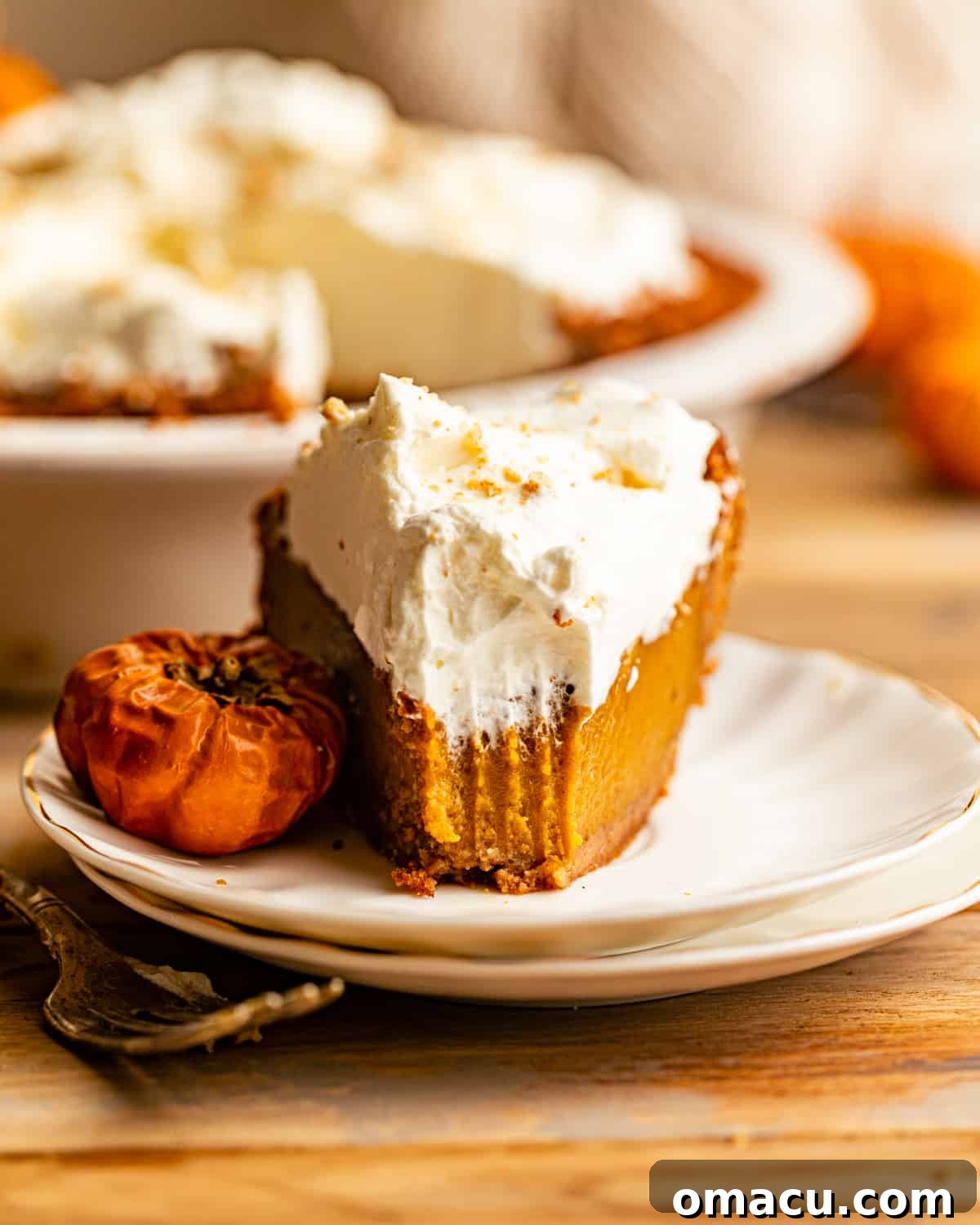 A perfectly sliced piece of pumpkin pie with whipped cream on a white plate, ready to be enjoyed.