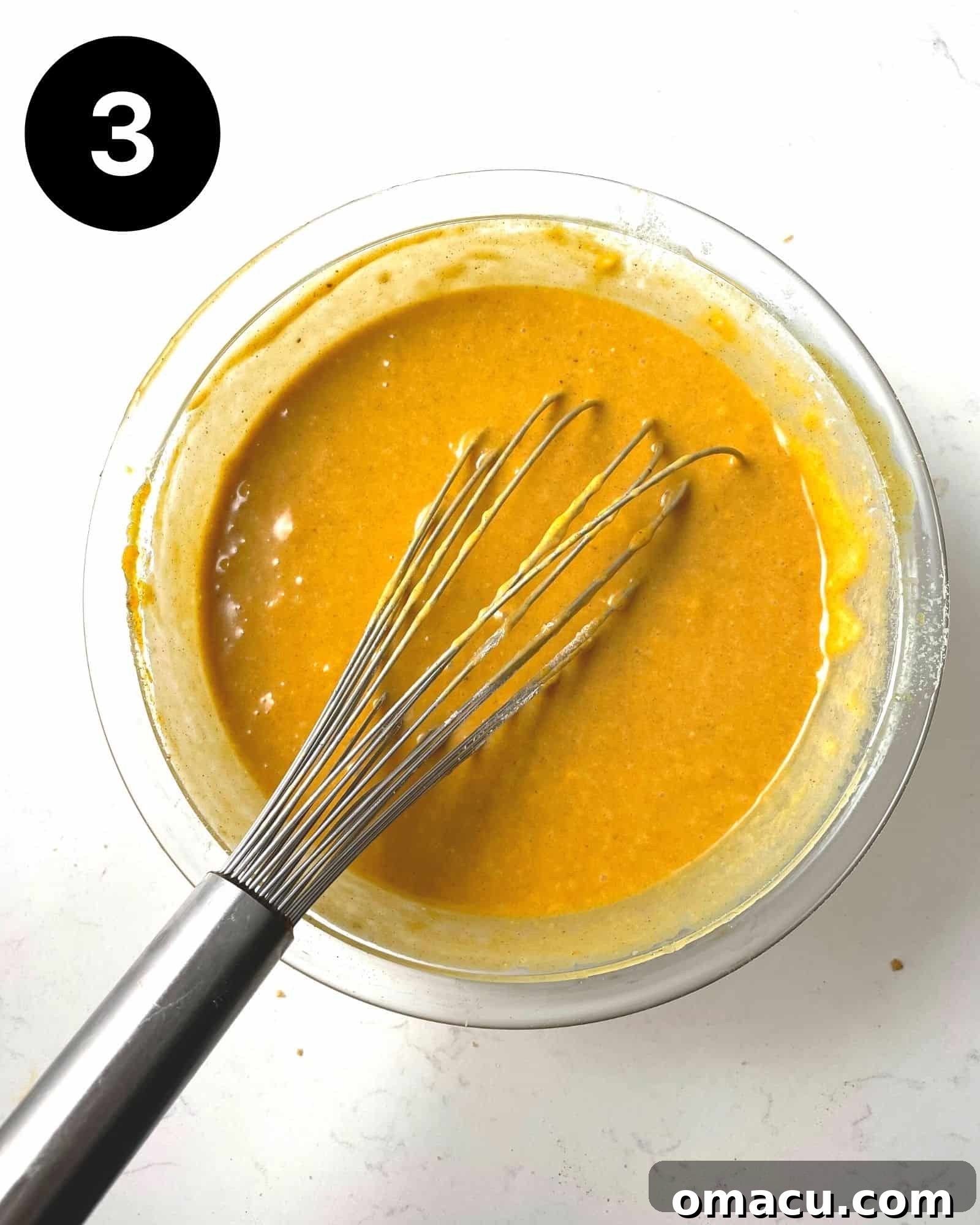 Smooth, orange pumpkin pie filling in a glass mixing bowl, ready to be poured into the crust.