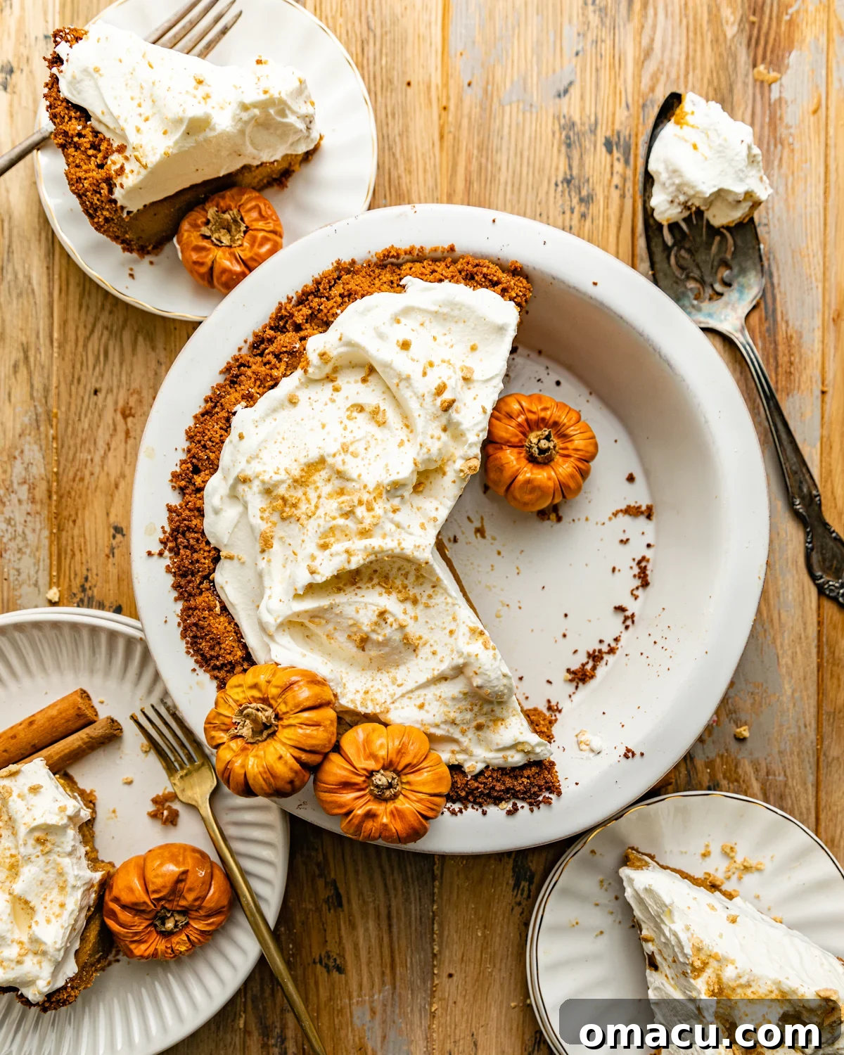 A full pumpkin pie with graham cracker crust in a pie dish, garnished with whipped cream and a sprinkle of cinnamon.