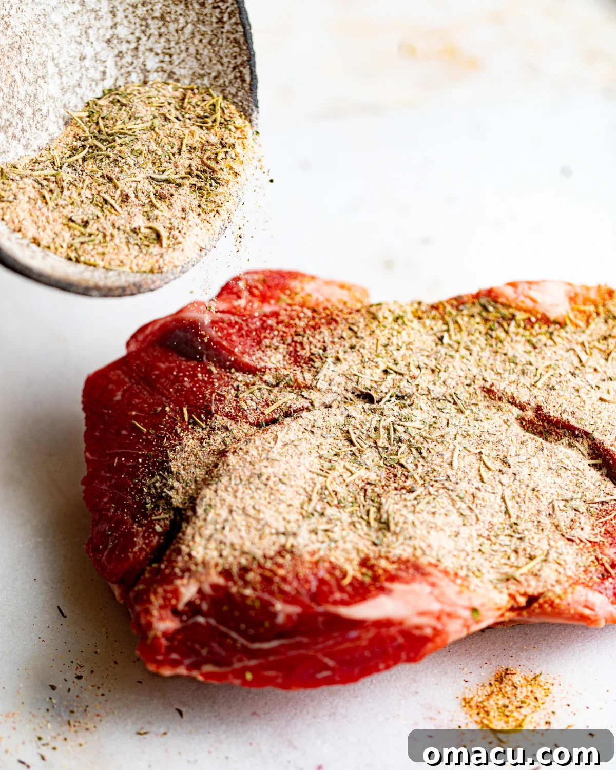 A raw chuck roast liberally coated in homemade pot roast seasoning, ready for cooking.