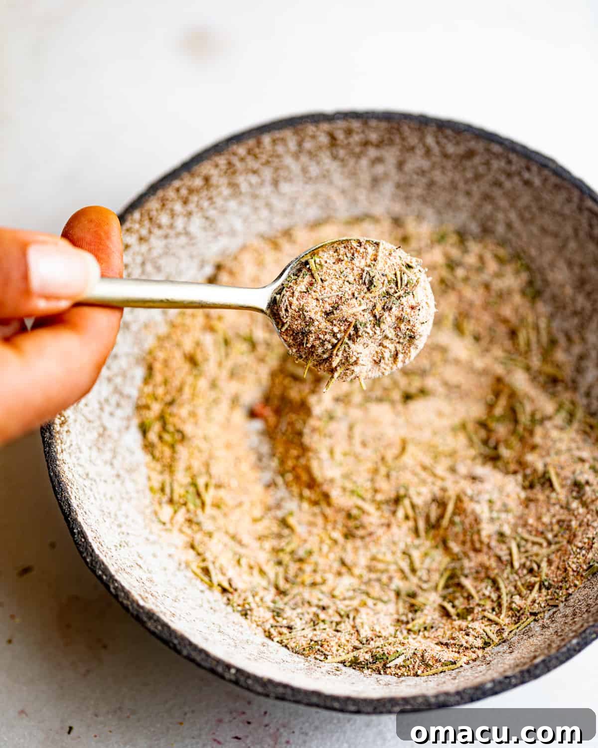 A spoon mixing various spices in a bowl to create the pot roast seasoning.