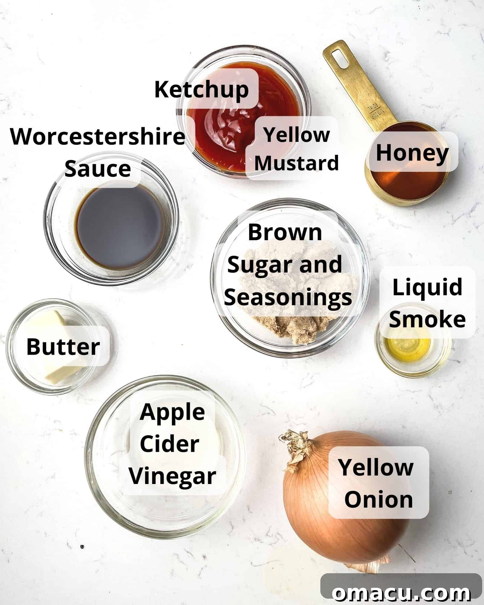 A vibrant display of ingredients for honey bbq sauce, including a yellow onion, a jar of honey, Worcestershire sauce, liquid smoke, a bottle of ketchup, apple cider vinegar, brown sugar, smoked paprika, chili powder, black pepper, yellow mustard, and butter.