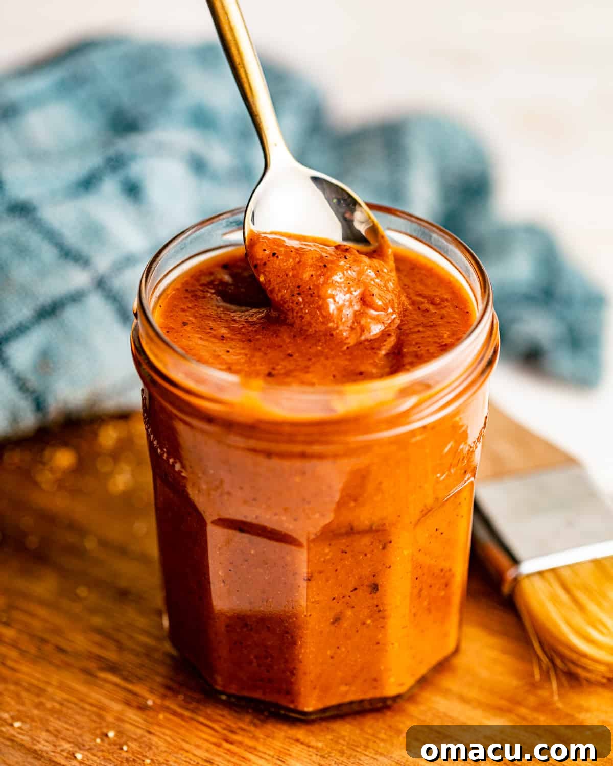 A rustic serving board featuring a bowl of rich, smooth honey bbq sauce with a spoon, highlighting its inviting texture.