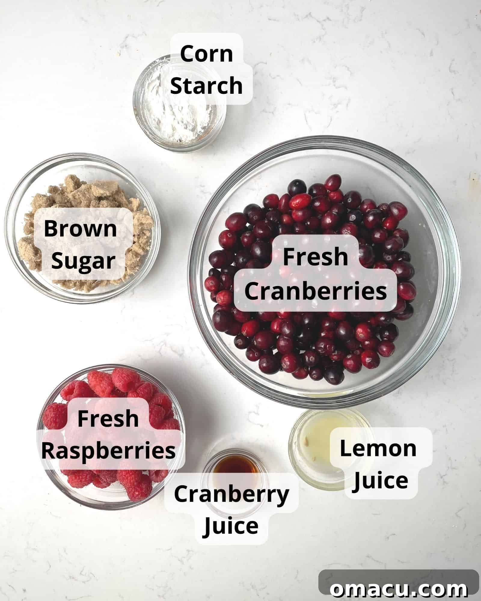 Essential ingredients laid out for making cranberry raspberry sauce: fresh cranberries, fresh raspberries, lemon, cranberry juice, brown sugar, and cornstarch.
