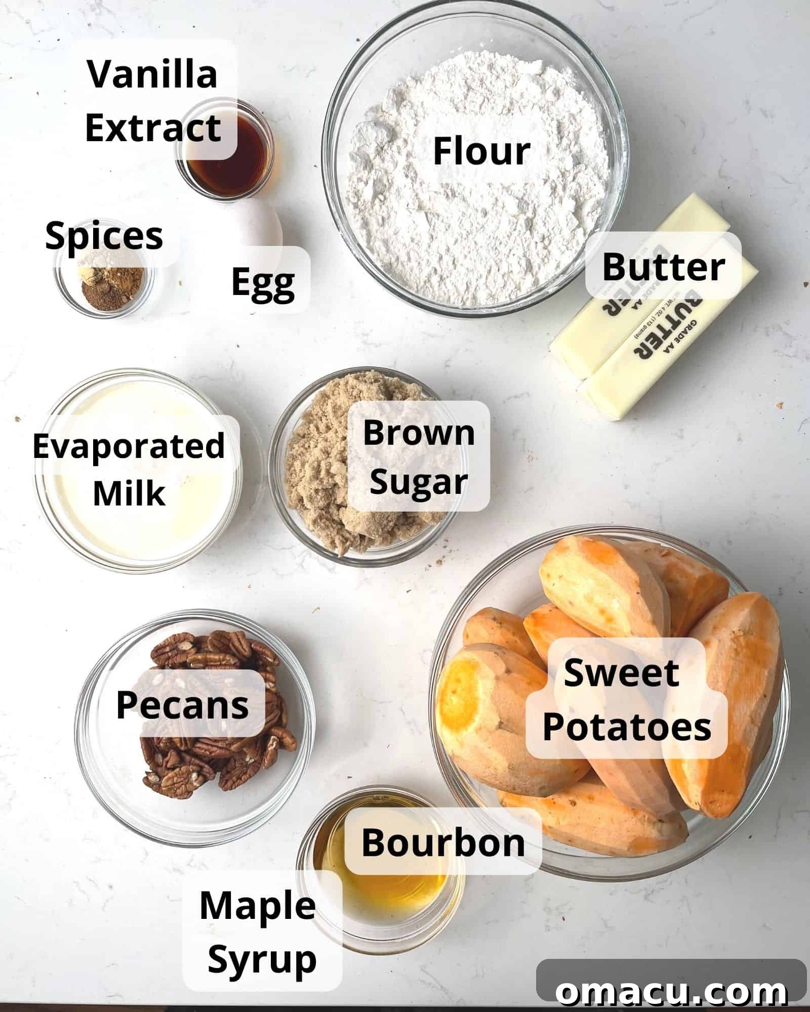 A beautiful flat lay of fresh ingredients for Bourbon Sweet Potato Casserole, including bright orange sweet potatoes, butter, pecans, brown sugar, various spices, a bottle of bourbon, maple syrup, evaporated milk, vanilla extract, and an egg.