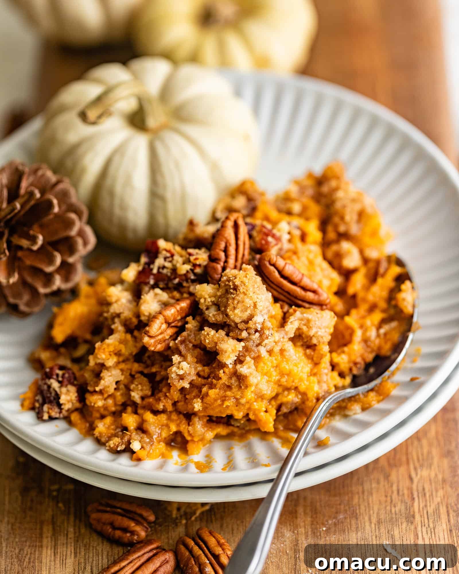 A tempting serving of Bourbon Sweet Potato Casserole on a white plate, showcasing its creamy interior and crunchy pecan streusel topping, garnished with a sprig of fresh herb.