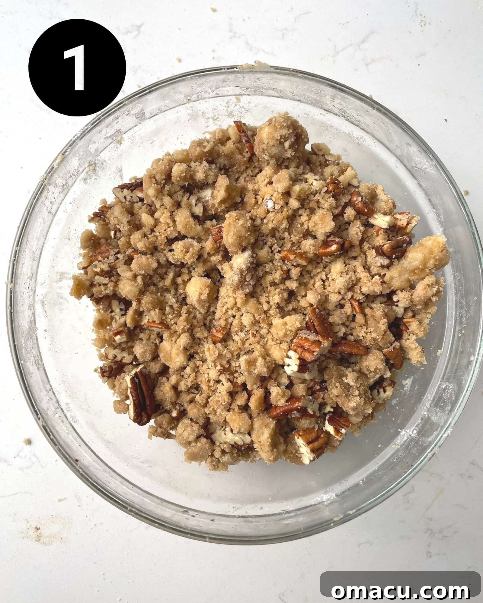 A close-up shot of the pecan streusel mixture in a small mixing bowl, showing the crumbly texture before chilling.