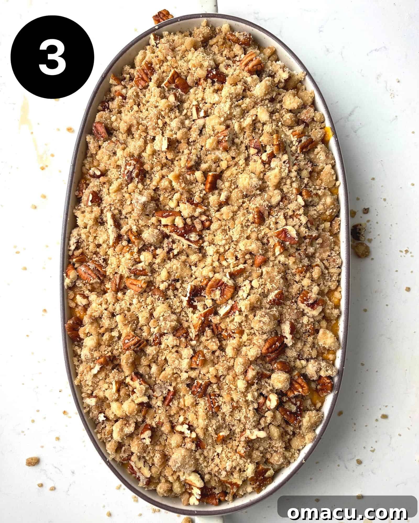 The assembled sweet potato casserole with a generous layer of pecan streusel topping, nestled in a baking dish, ready to be placed in the oven.