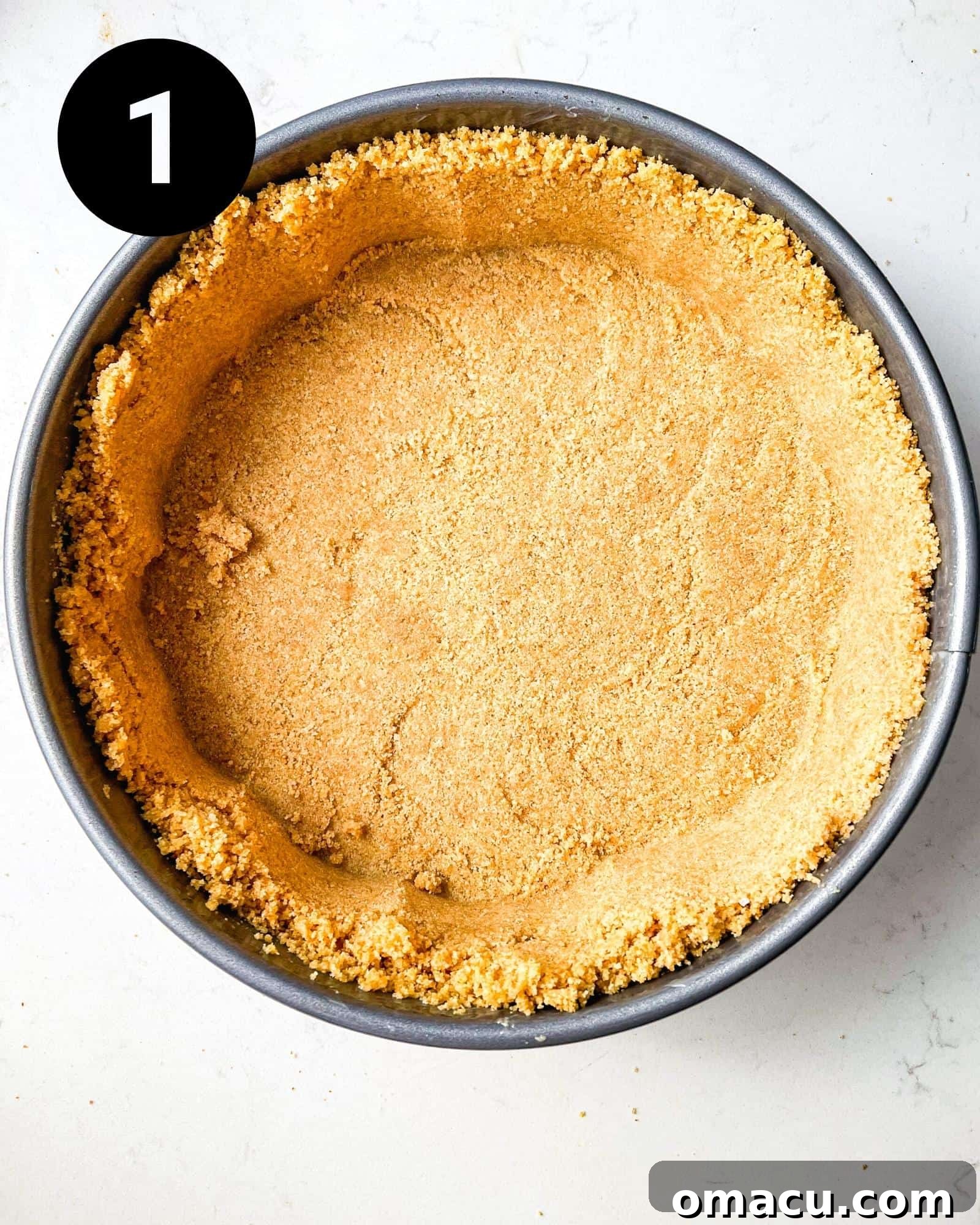 A golden-brown graham cracker crust neatly pressed into a 9-inch springform pan, chilling to set.
