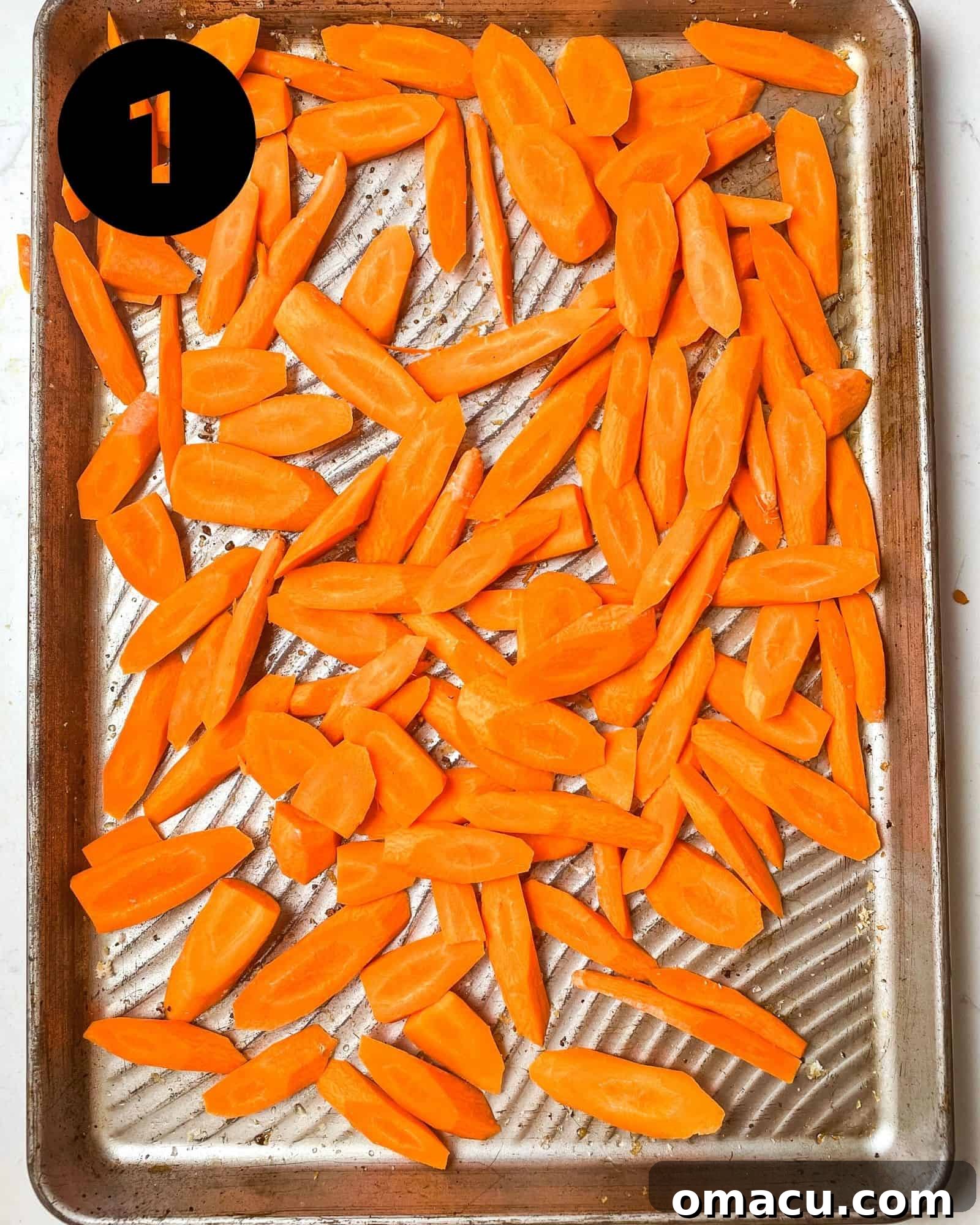 Uniformly sliced carrots spread in a single layer on a parchment-lined baking sheet, ready for seasoning.