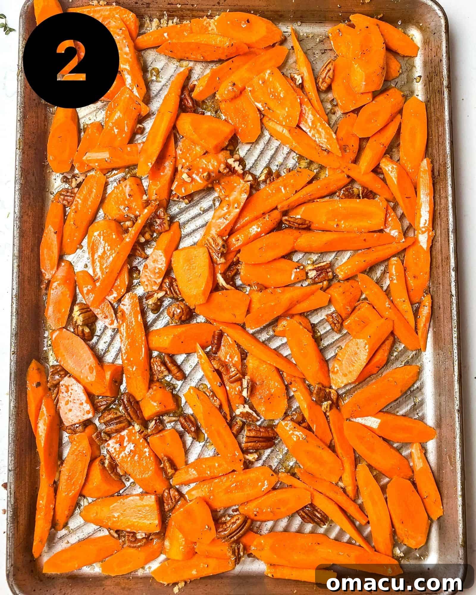 Sliced carrots on a baking sheet, coated with brown sugar, honey, fresh thyme, olive oil, and chopped pecans, tossed together.