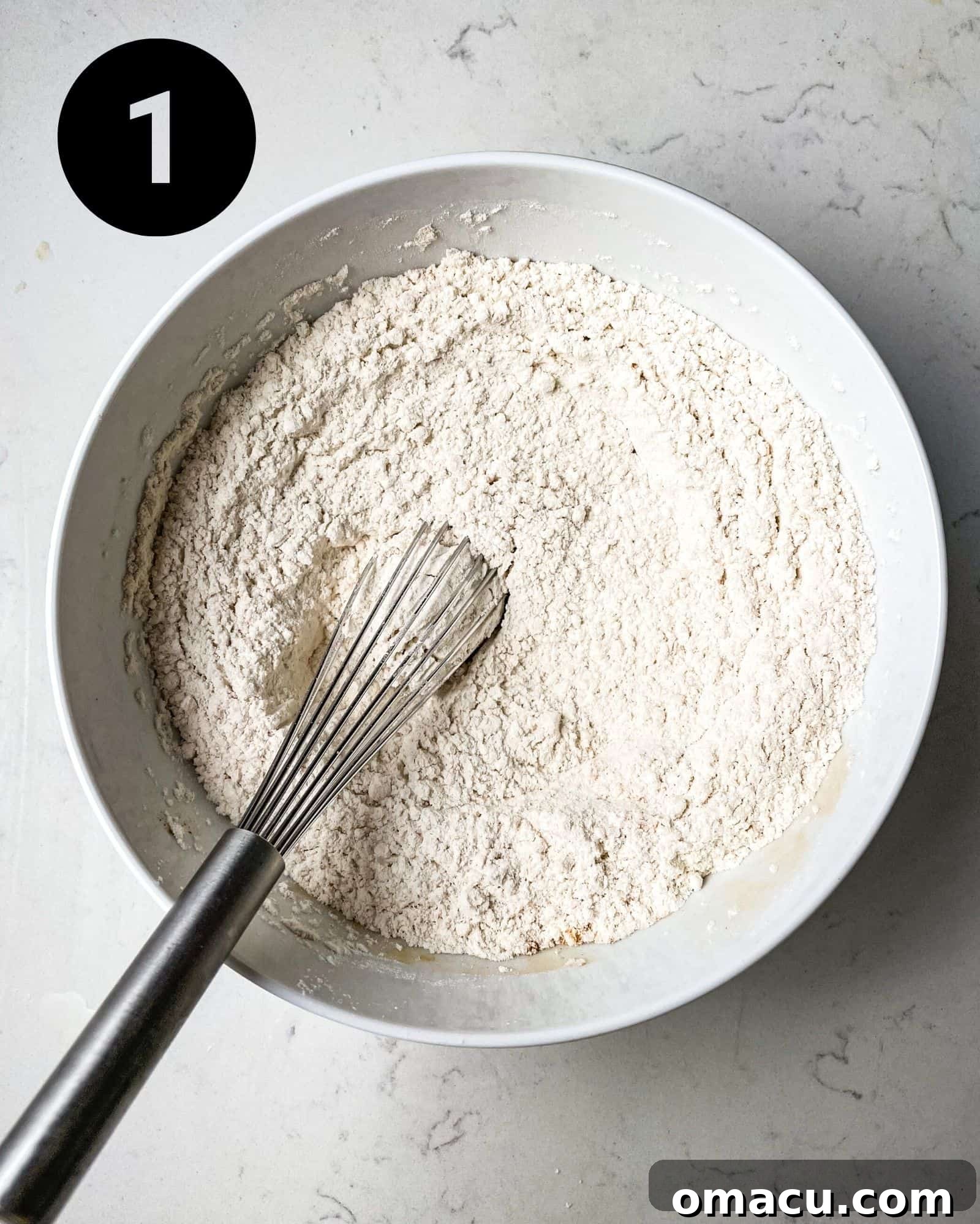 Dry ingredients for cardamom cake, including flour, baking powder, baking soda, cornstarch, salt, and ground cardamom, whisked together in a mixing bowl.