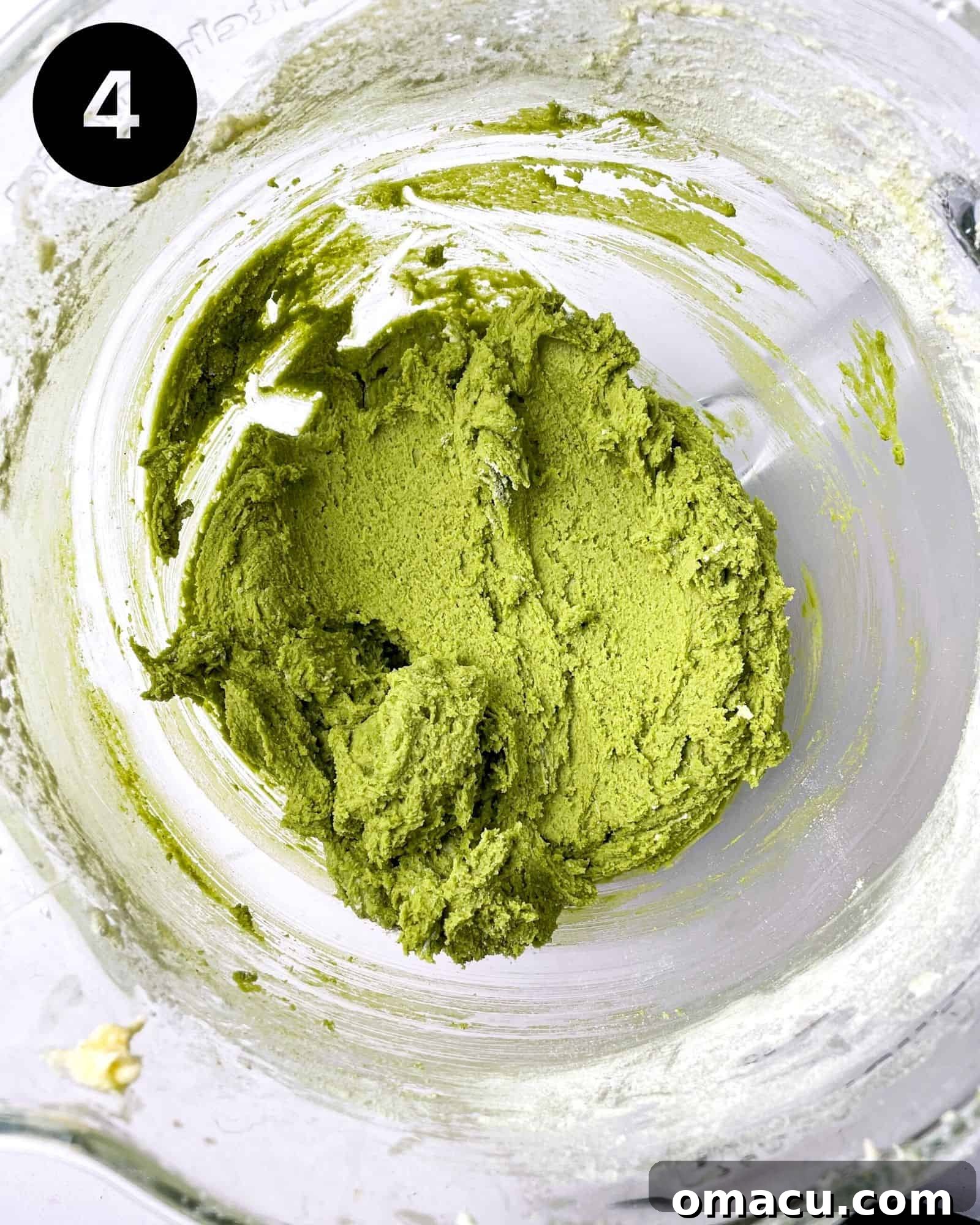 Close-up of butter, sugar, and matcha being creamed together in a mixing bowl, creating a smooth, light green mixture.