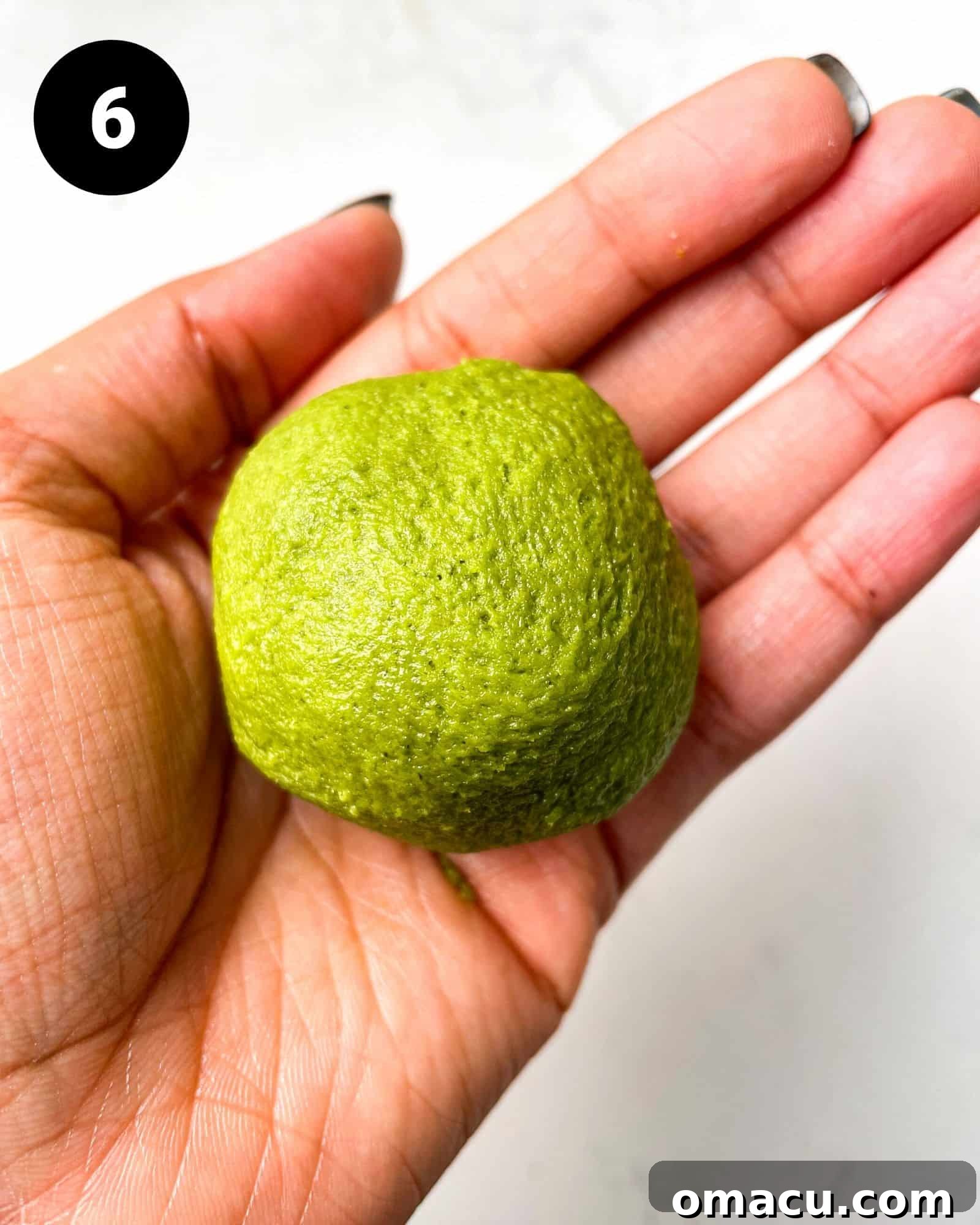 A perfectly rolled matcha cookie dough ball, with the white chocolate cream cheese filling fully encased within its vibrant green exterior.