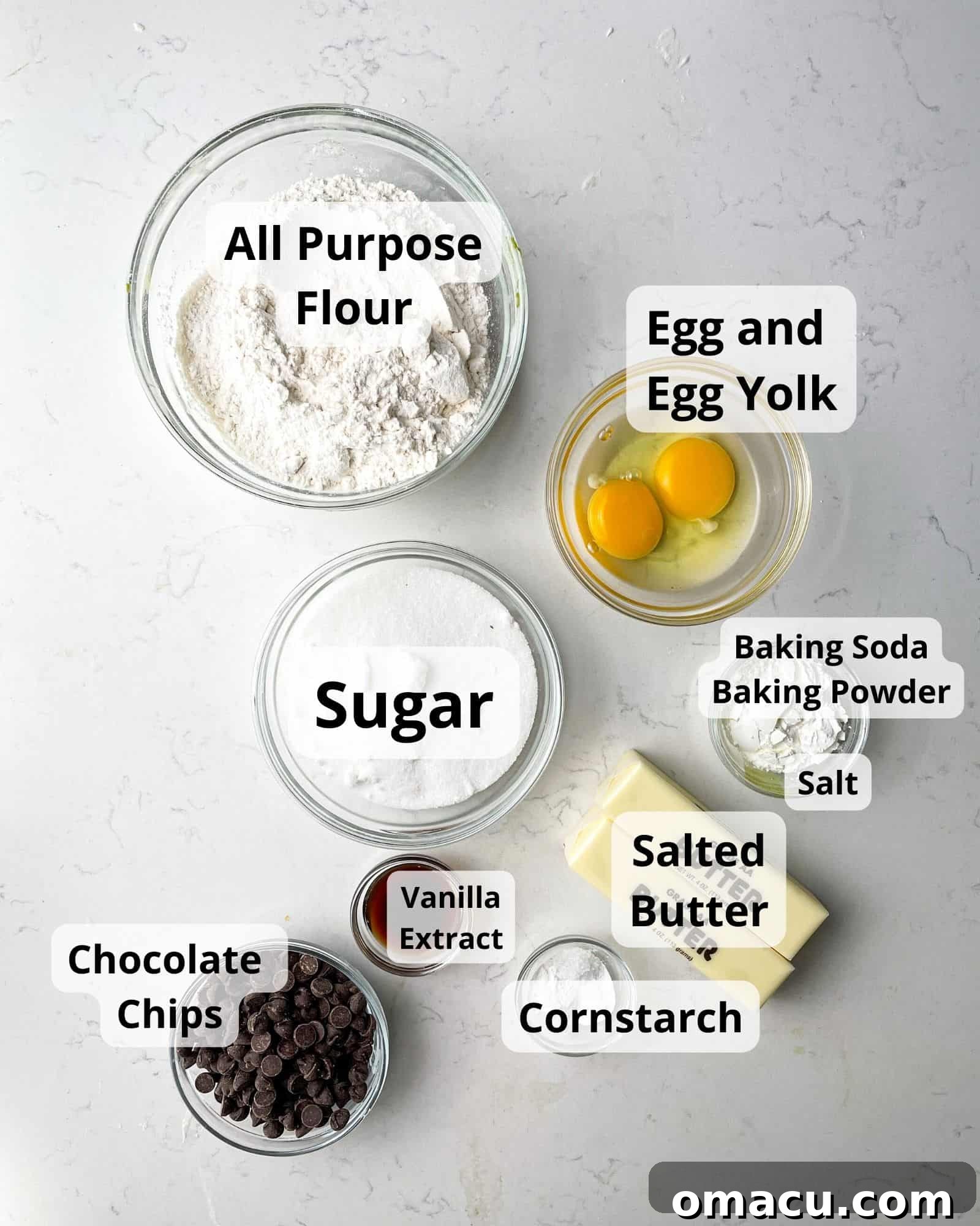 Assortment of key ingredients for chocolate chip sugar cookies: flour, egg, egg yolk, granulated sugar, chocolate chips, butter, cornstarch, baking powder, baking soda, and salt, artfully arranged on a kitchen counter.