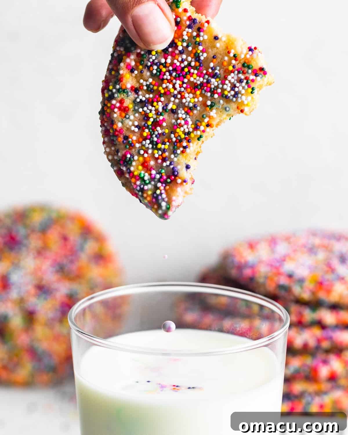 A close-up shot of a colorful sprinkle sugar cookie being dipped into a refreshing glass of milk, emphasizing its soft texture and the delightful visual of the sprinkles.