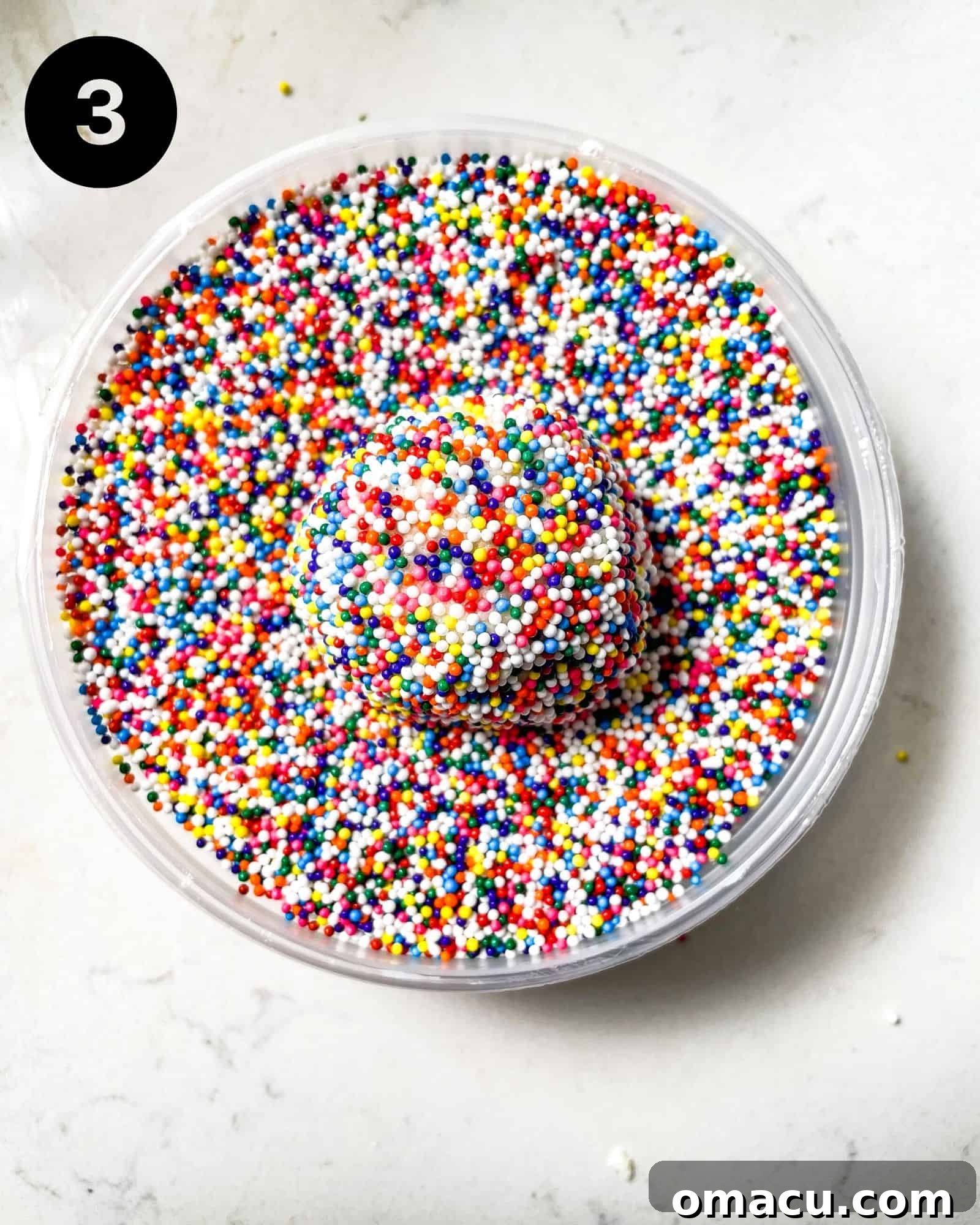 A perfectly rolled cookie dough ball, completely coated in vibrant nonpareils sprinkles, ready to be placed on a baking sheet.