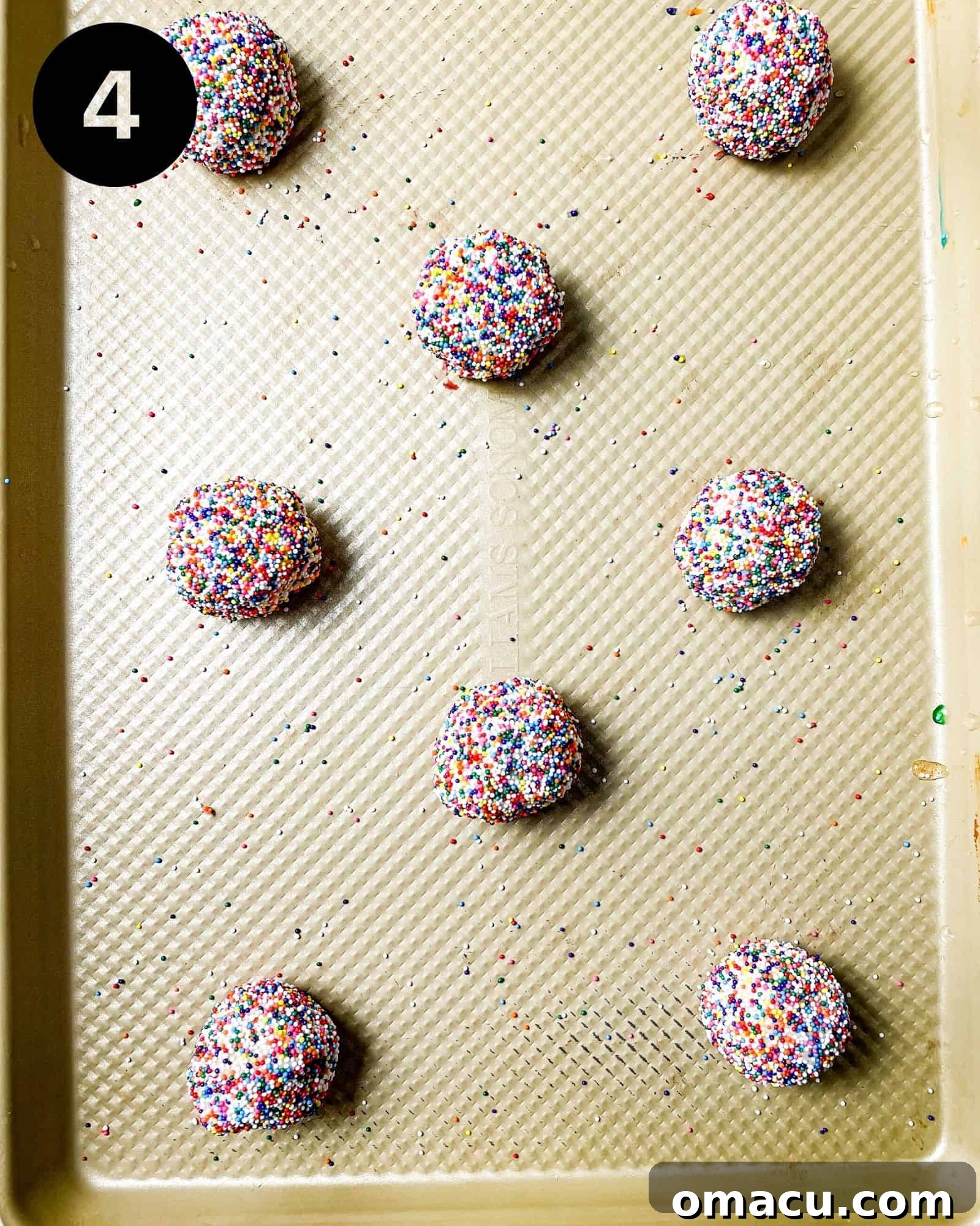 A baking sheet filled with evenly spaced, sprinkle-coated cookie dough balls, ready for the oven to transform them into delicious treats.