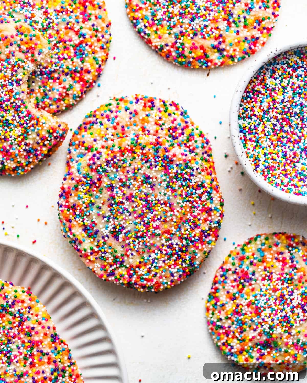 Freshly baked sprinkle sugar cookies arranged neatly on a pristine white surface, showcasing their vibrant colors and perfect round shape.