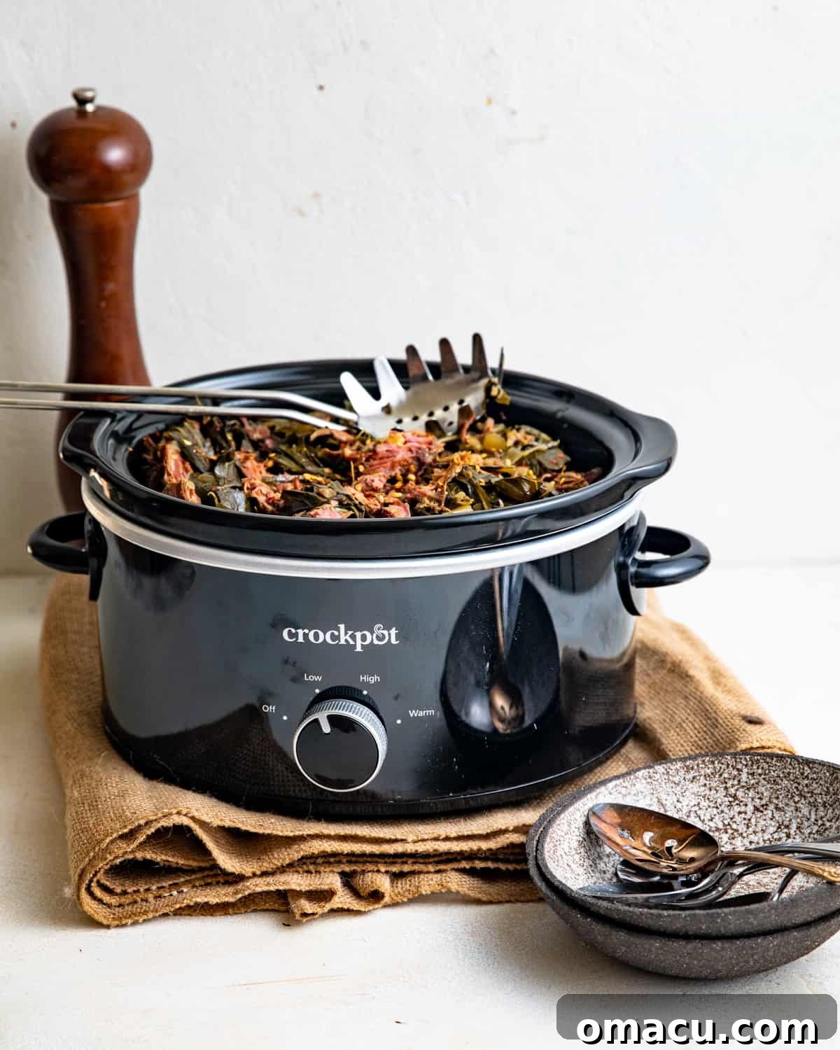 Fresh collard greens being loaded into a crockpot with smoked meat and broth.