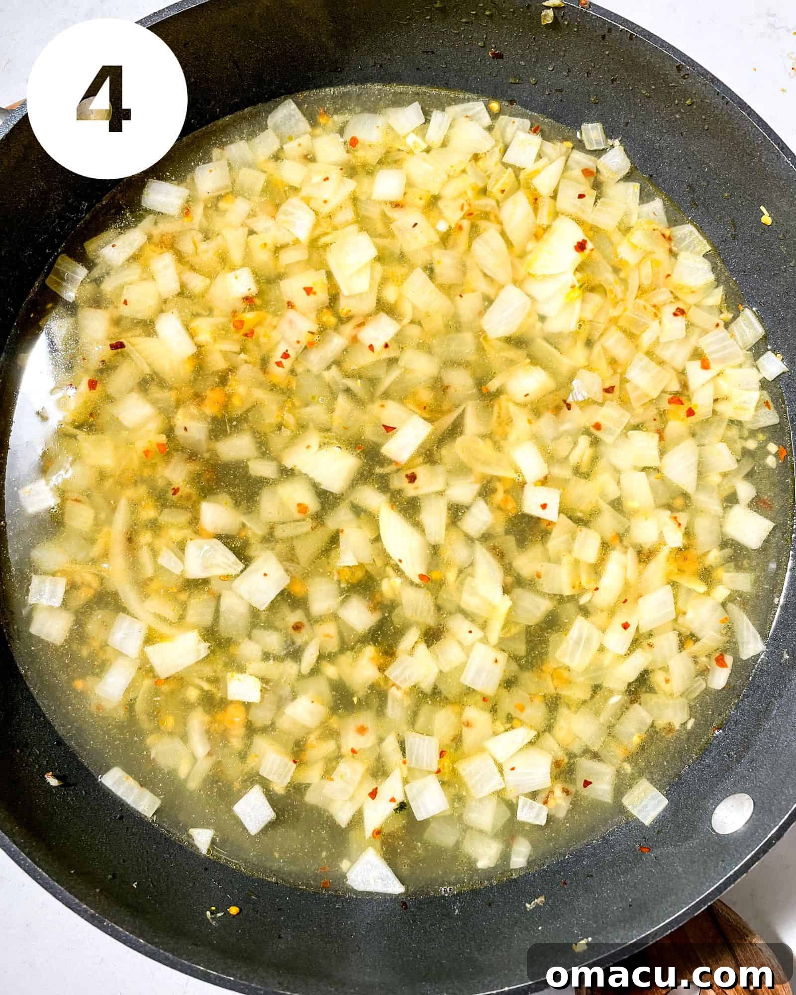 Chicken broth added to the pot with sautéed onions, garlic, and seasonings, creating a rich cooking liquid.