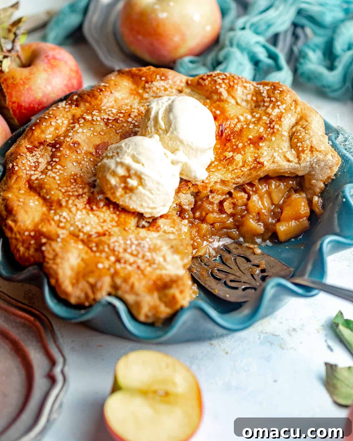 A delectable slice of maple apple pie, served in a pie plate and crowned with a scoop of melting vanilla ice cream, ready to be enjoyed.