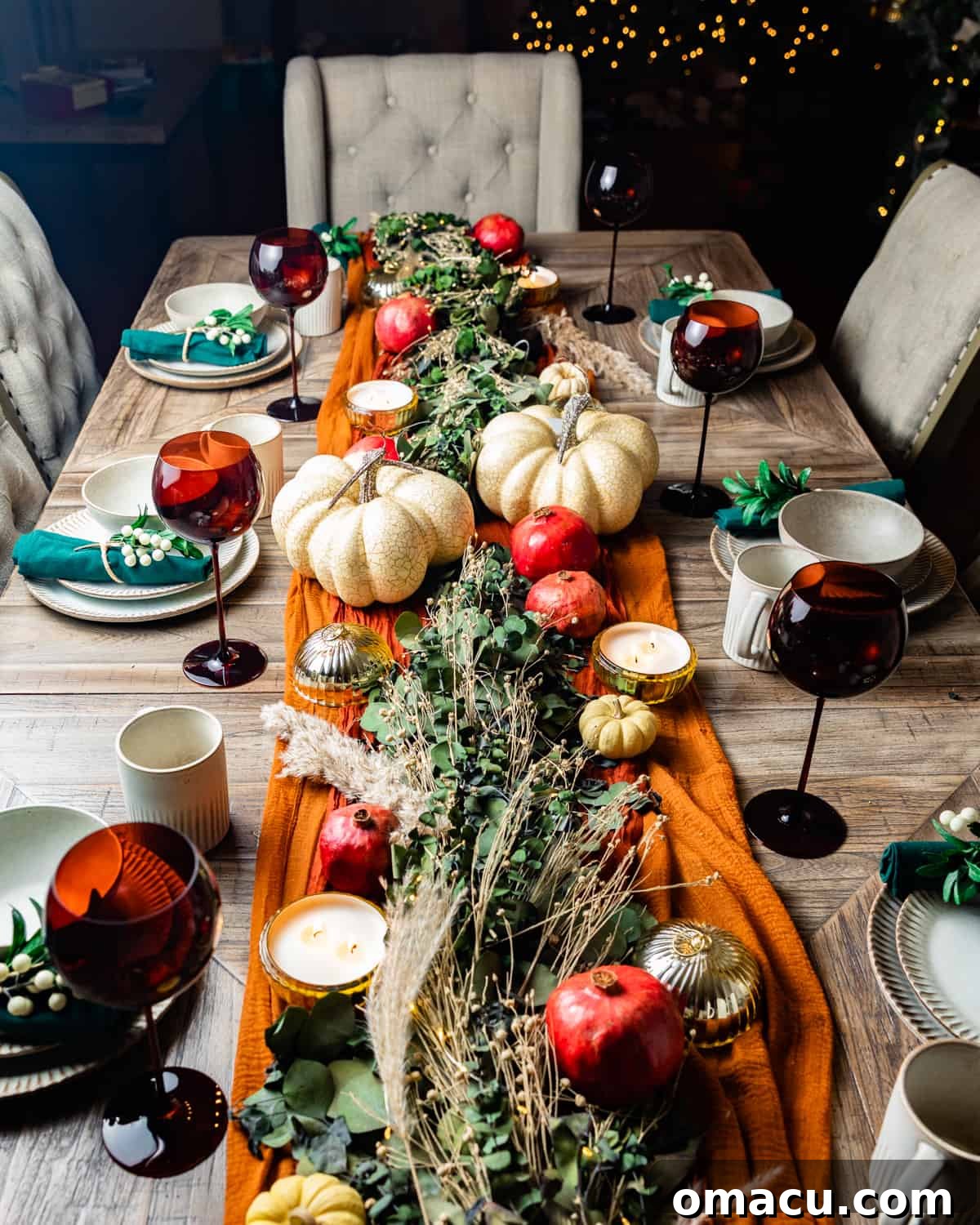 A beautifully arranged Thanksgiving table, adorned with a lush garland and decorative pumpkins, creating an inviting and festive atmosphere.