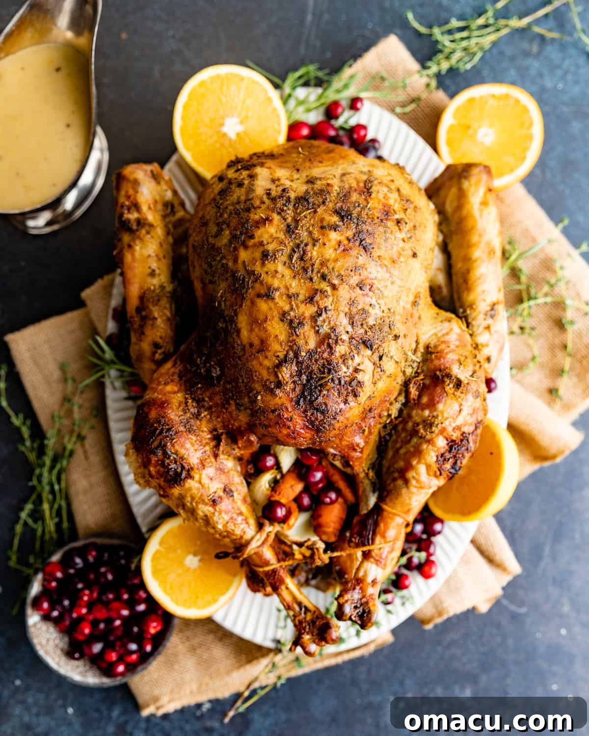 A majestic whole herb-roasted turkey, beautifully presented on a serving tray and elegantly garnished with fresh citrus fruits and fragrant herbs, ready for carving.