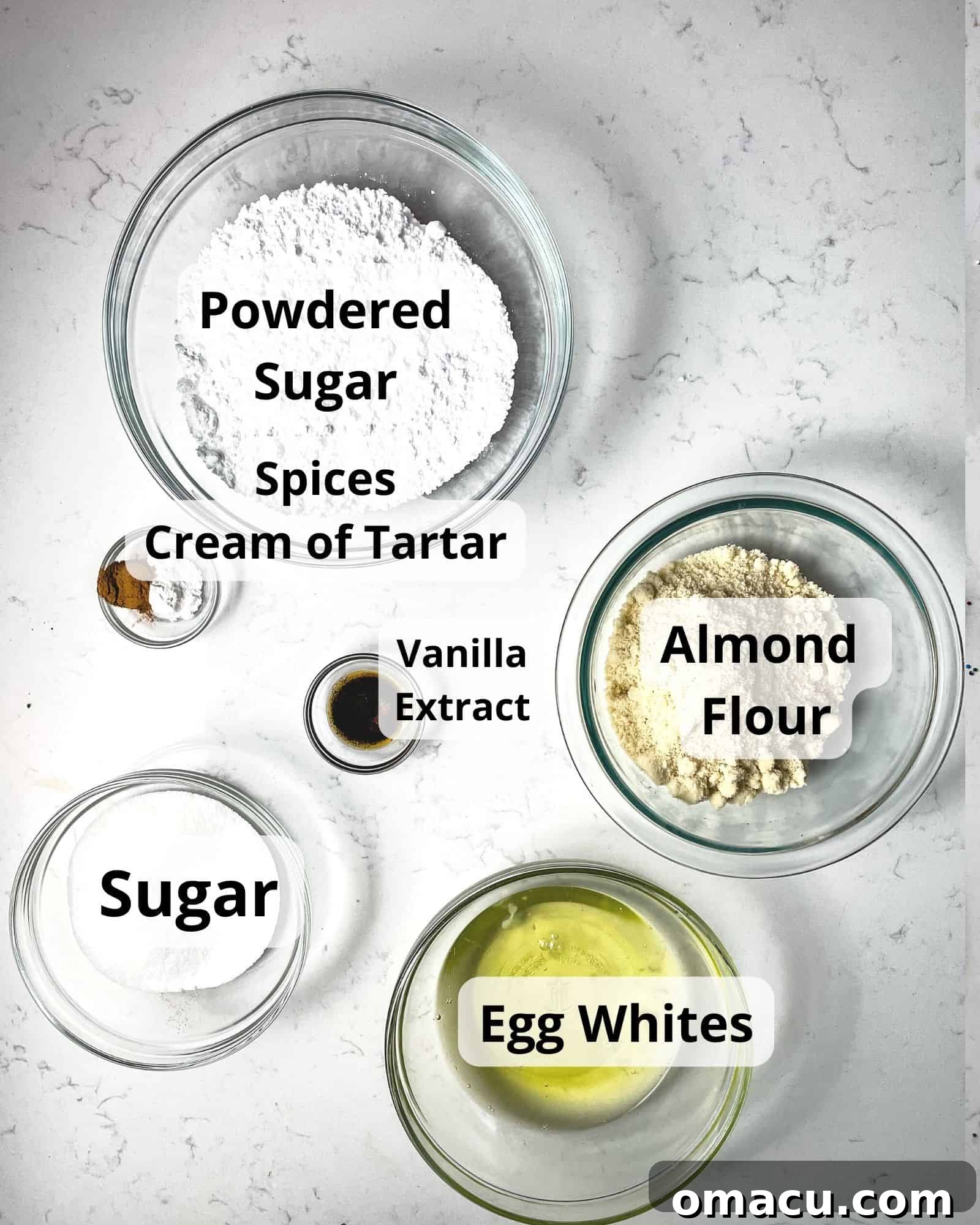 ingredients to make gingerbread macarons - egg whites, powdered sugar, vanilla extract, granulated sugar, almond flour, cream of tartar, and various spices.