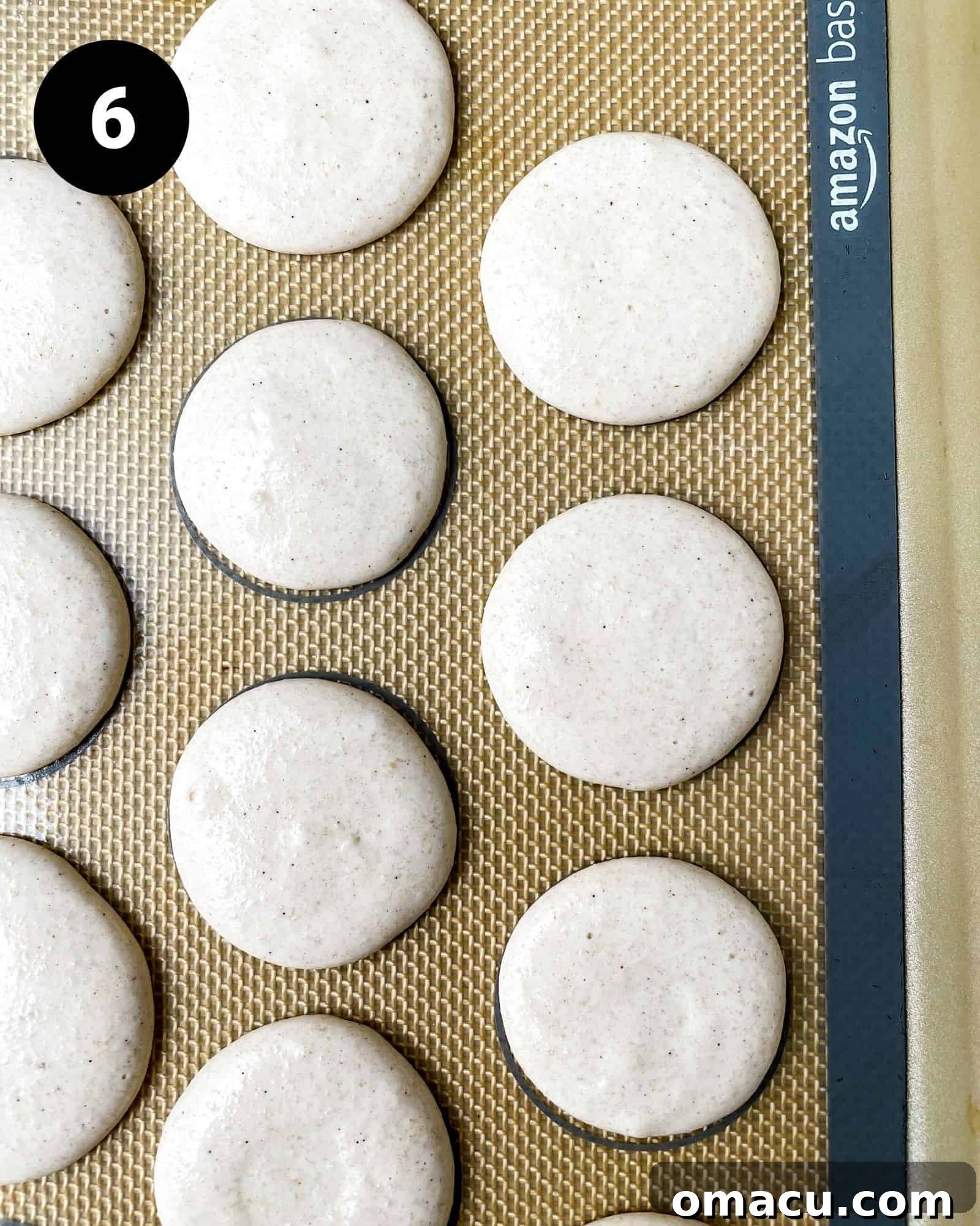 gingerbread macaron shells neatly piped onto a silicone baking mat, ready for drying.