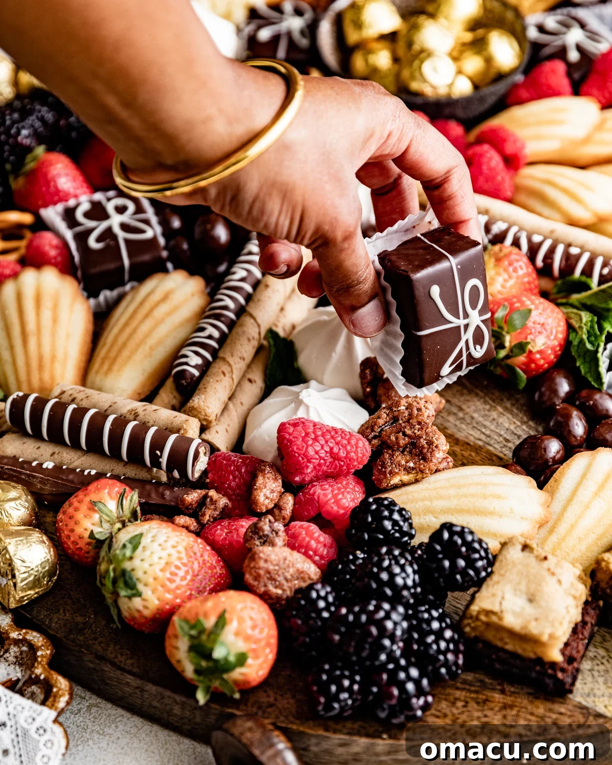 A hand reaching for a chocolate truffle from a bountiful dessert charcuterie board, showcasing the interactive nature of the sweet spread.