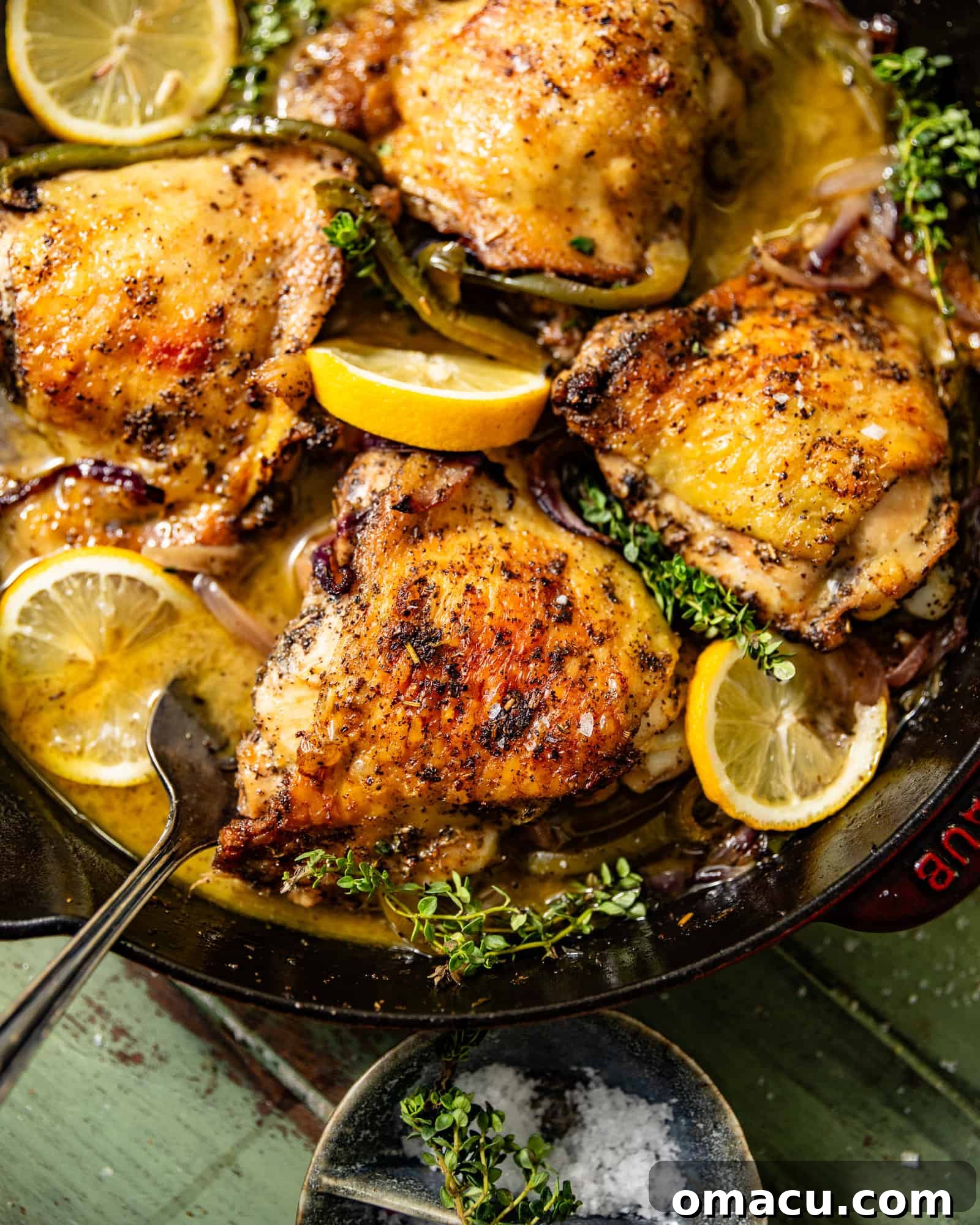 Beautifully seared chicken thighs in a cast iron skillet, garnished with fresh herbs and lemon slices, ready for the oven.