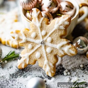 A beautifully decorated snowflake shortbread cookie placed in front of a festive teacup filled with Christmas ornaments, capturing the essence of holiday baking.
