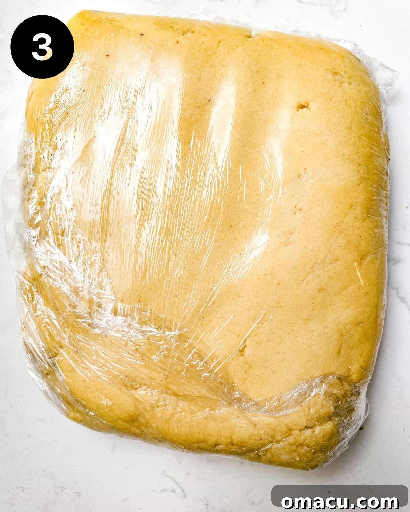 The prepared shortbread cookie dough is covered securely with plastic wrap, ready for chilling in the refrigerator to firm up before rolling and cutting.