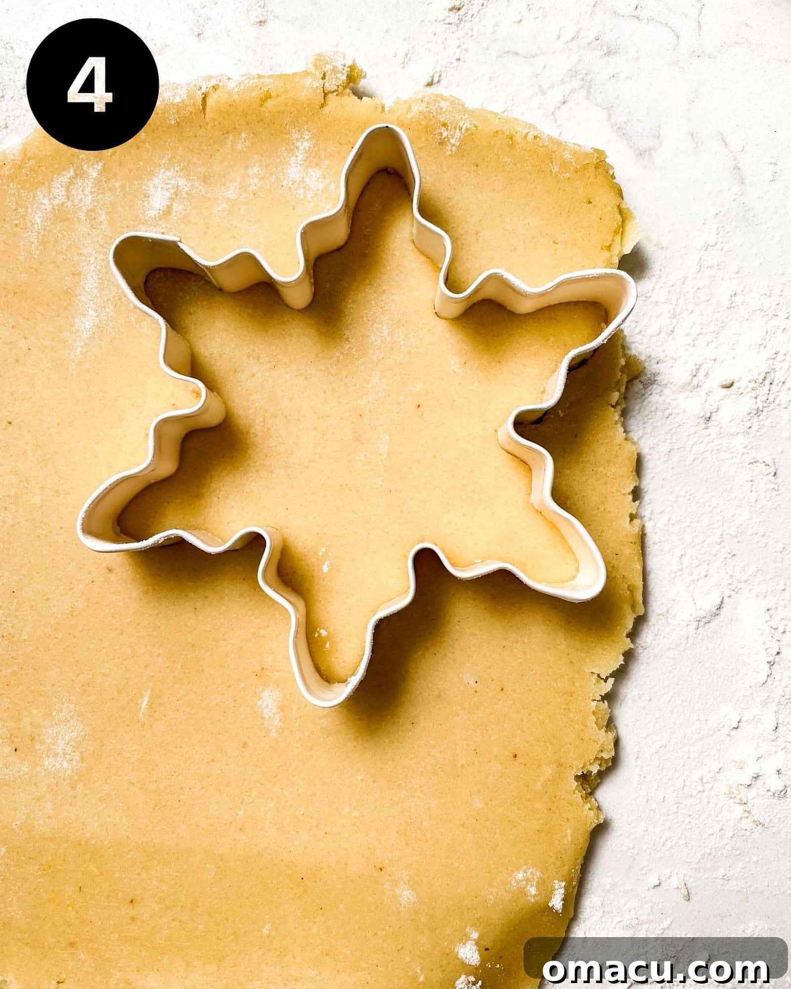Chilled shortbread cookie dough is rolled out on a lightly floured surface, with a snowflake cookie cutter pressed into it, demonstrating the precise cutting process.
