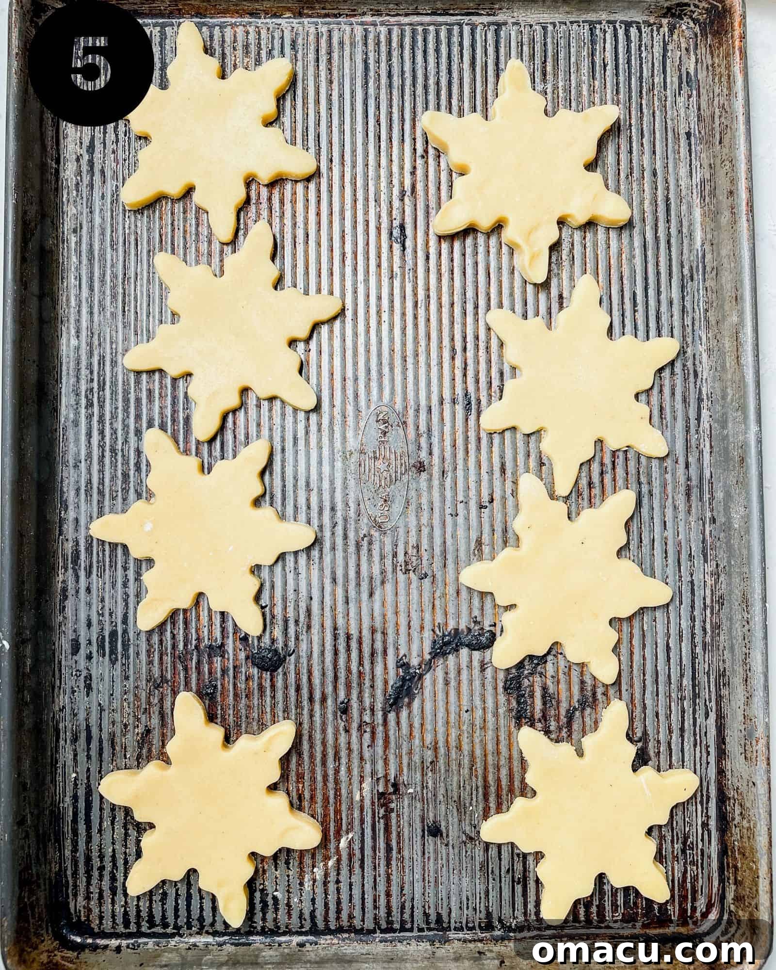 A baking sheet filled with freshly cut snowflake shortbread cookies, perfectly spaced and ready to be placed into the preheated oven.
