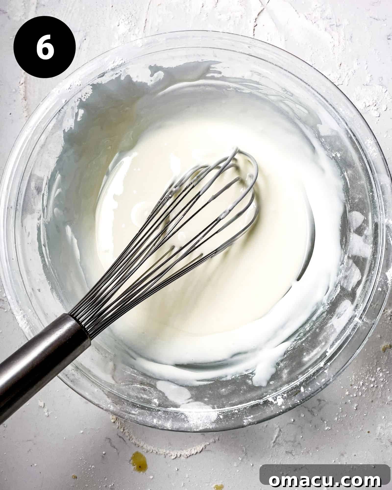 Smooth, white royal icing is whisked to the perfect consistency in a mixing bowl, ready for decorating the snowflake cookies.