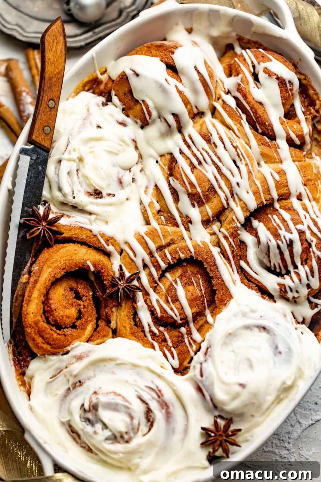 Freshly baked homemade cinnamon rolls in a baking dish, generously covered in creamy, white cream cheese icing.