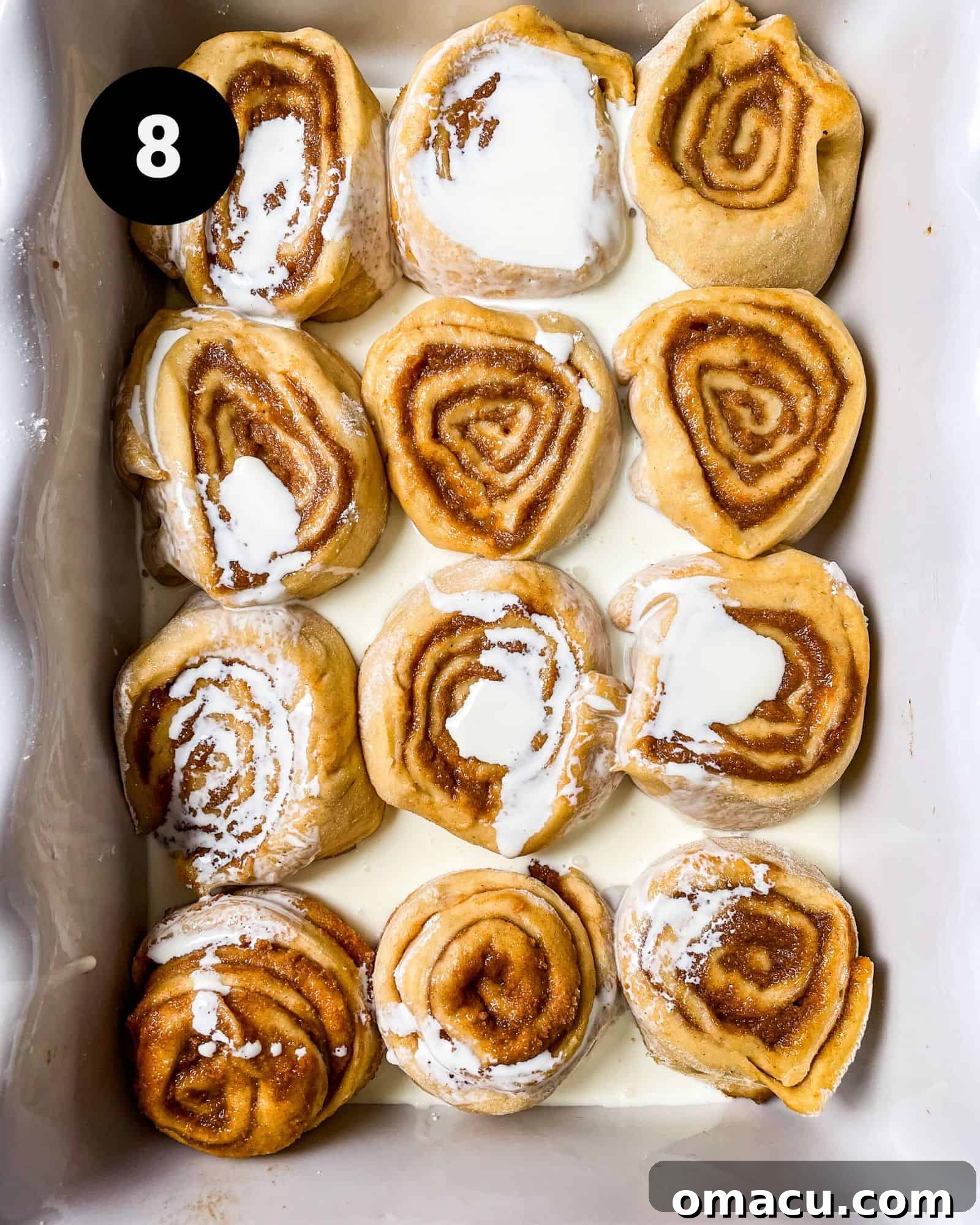 Cinnamon rolls in a baking dish with heavy cream poured over them, just before going into the oven.