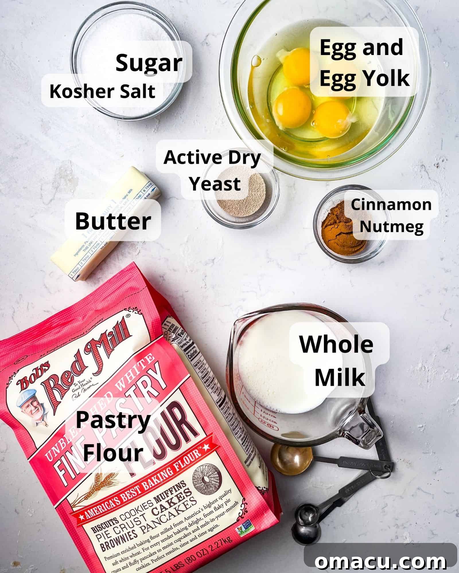 A vibrant flat lay of all the essential ingredients needed to make homemade cinnamon rolls: pastry flour, butter, sugar, salt, active dry yeast, whole milk, cinnamon, nutmeg, eggs, and egg yolks.