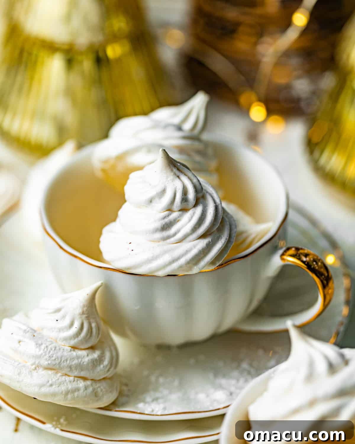 meringue kisses inside of a teacup on top of a tea plate. Beautifully piped meringue kisses, perfectly baked with a crisp, ethereal quality, elegantly arranged within a vintage teacup on a matching tea plate, ready for serving.