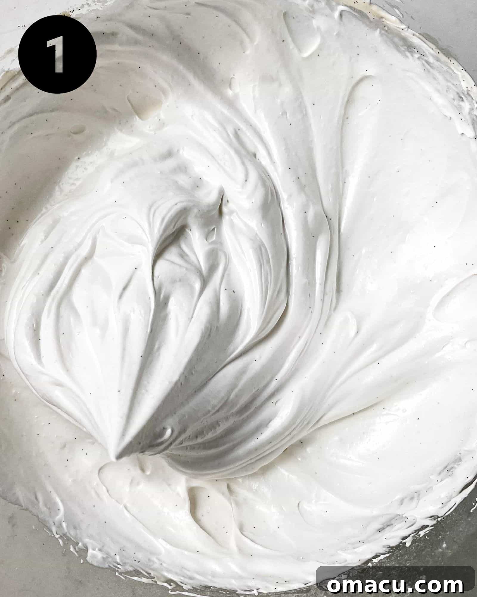 meringue in a mixing bowl. Egg whites and sugar have been whipped to a stiff peak, forming a glossy white meringue ready for piping.