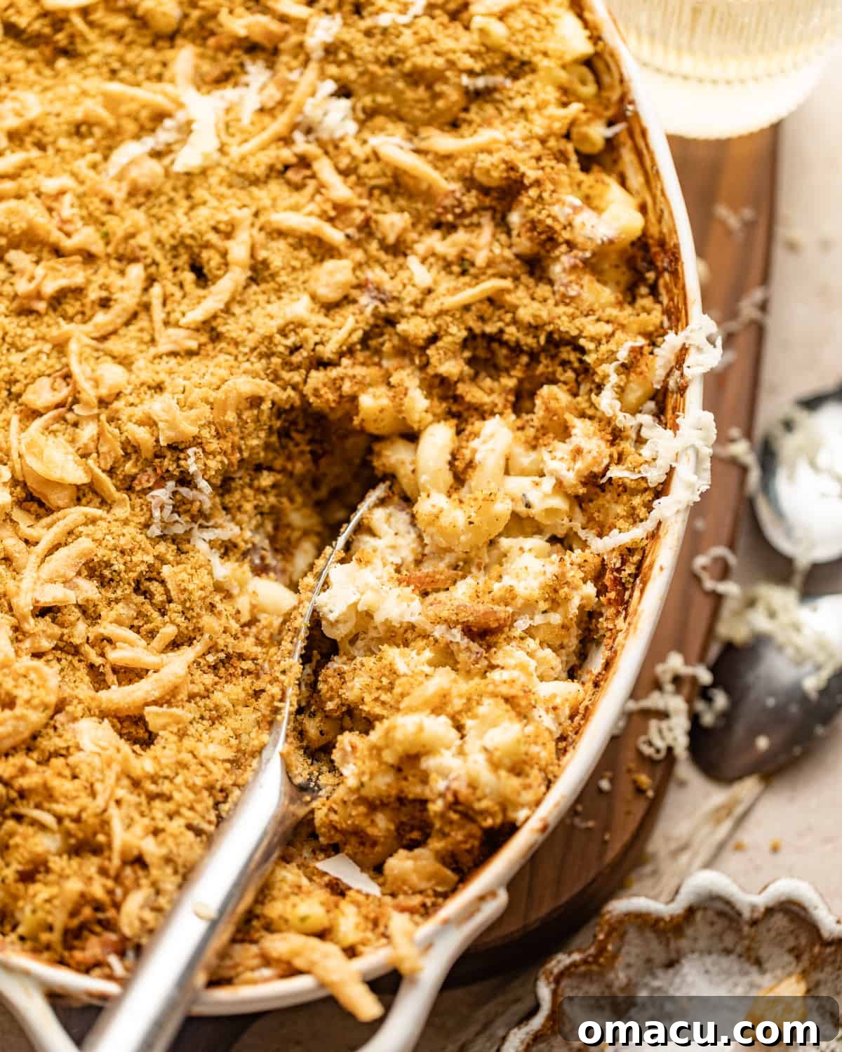 An inviting close-up photo of a spoon expertly scooping a generous portion of creamy prosciutto mac and cheese out of a bubbling baking dish, showcasing its rich texture and golden topping.