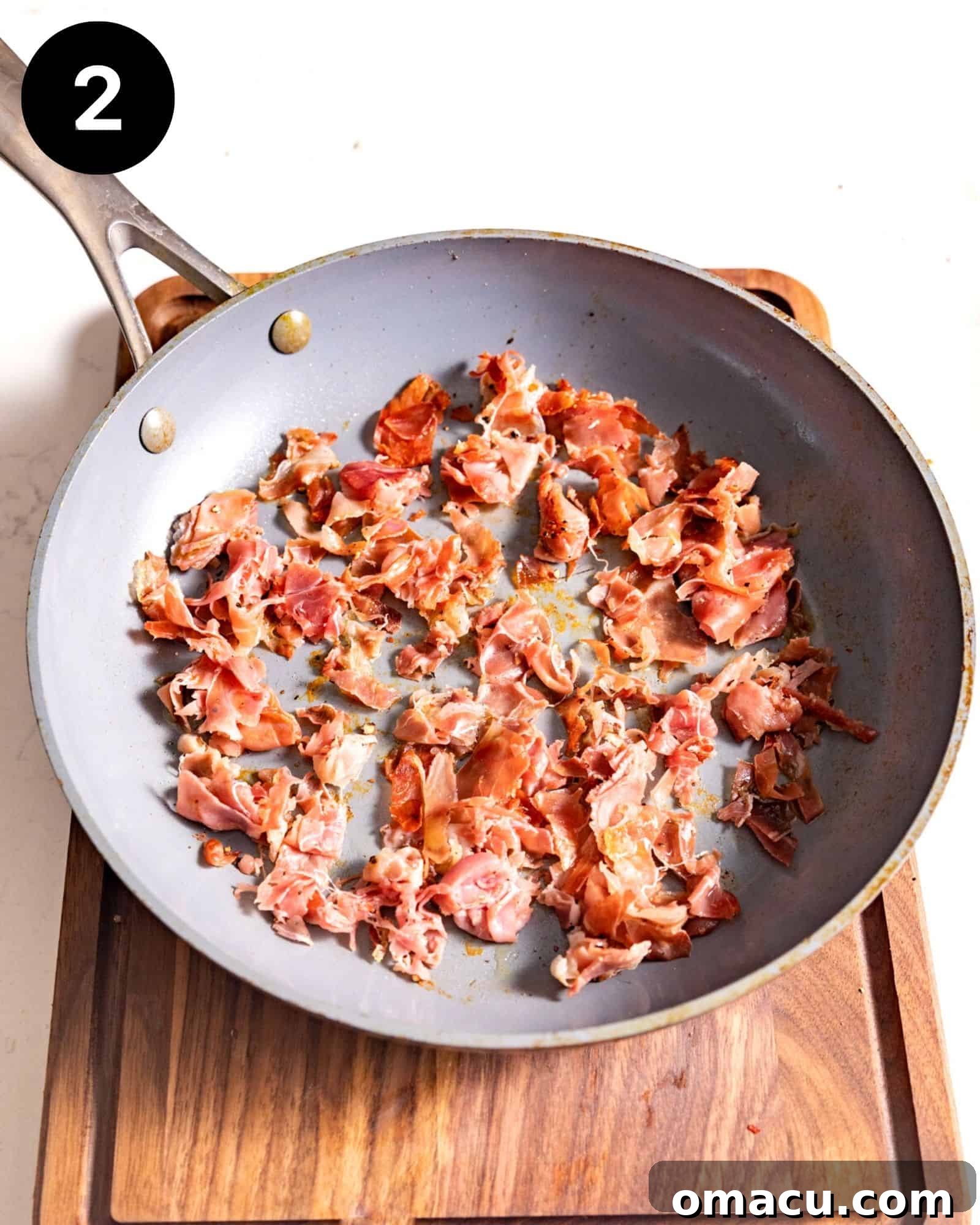 Crispy, golden-brown prosciutto sizzling gently in a frying pan, releasing its irresistible aroma and preparing for incorporation into the mac and cheese.